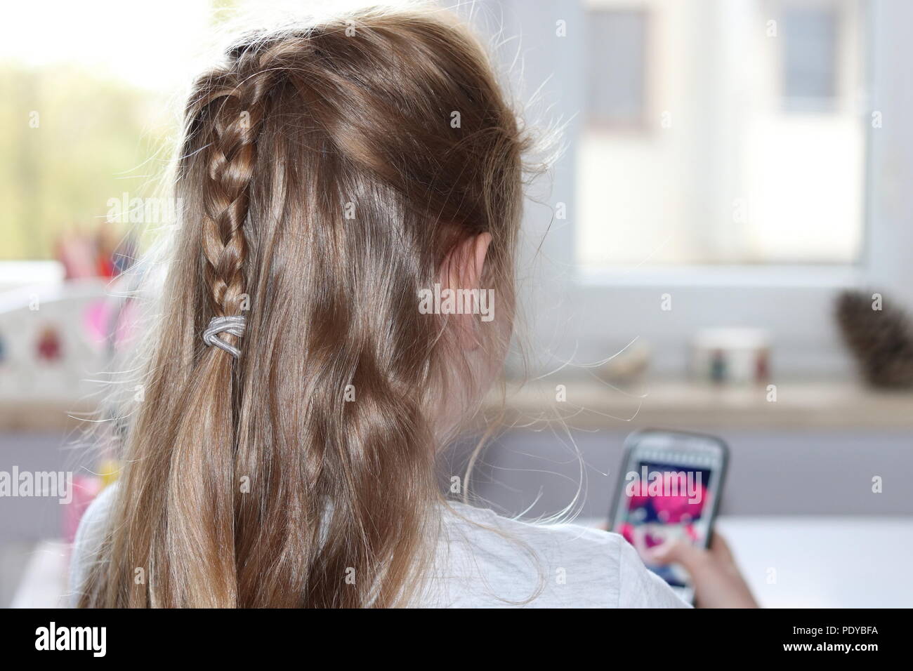 Blond teenager girl (upper part of body) sist on her back, holds smartfon in hand and look at phone screen, room interior Stock Photo