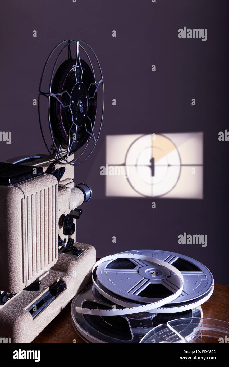 Film show. Old mid 1960s Eumig P8 home movie projector showing a cine film with spools of films next to it. Stock Photo