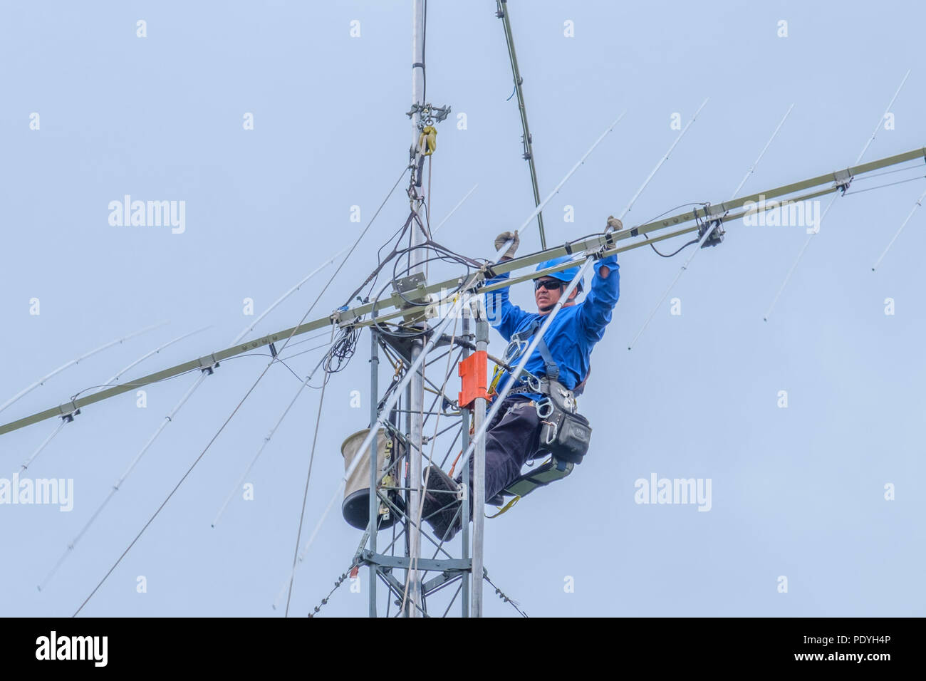 Telecom tower climber working on top of radio tower installing a amateur radio shortwave directional antenna. Stock Photo