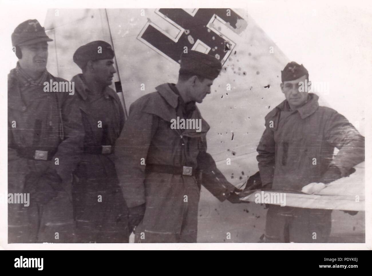 Image from the photo album of Feldwebel Willi Hoffmann of 5. Staffel, Kampfgeschwader 30: Willi Erkens and his crew from 5./KG 30 pose in front of their winter-camouflaged Junkers Ju 88 bomber, following a hit by Flak on the right stabiliser in the Winter of 1941-42. From left to right: Unteroffizier Otto Bienmüller (Radio Operator), Gefreiter Willi Hoffmann (Air Gunner), Feldwebel Willi Erkens (Pilot) and Feldwebel Richard Müller (Observer - standing in the hole caused by a shell). The entire crew failed to return from a mission in the Mediterranean on 23rd January 1943. Stock Photo