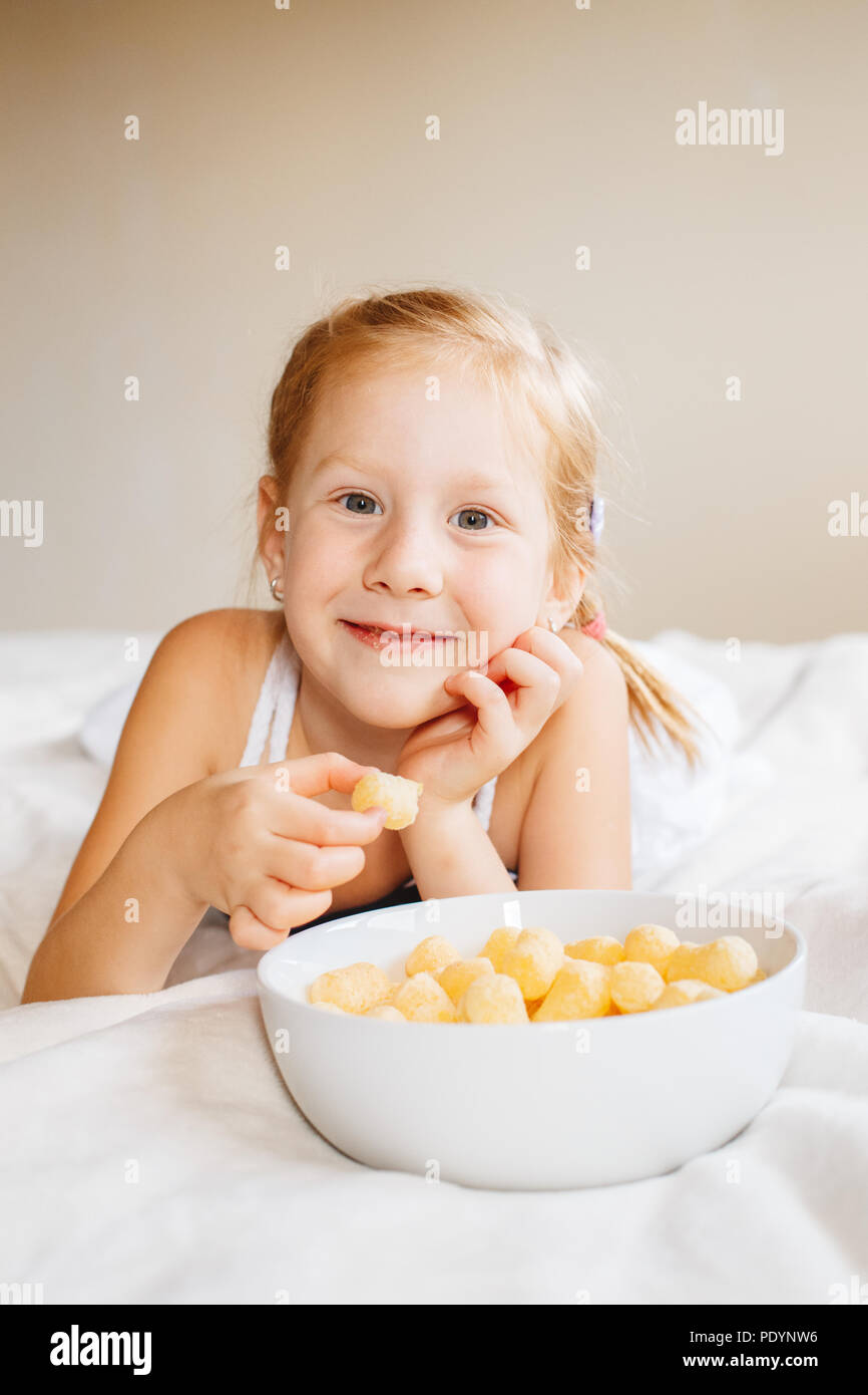 Portrait of one white Caucasian child girl smiling eating corn puffs. Preschooler kid eating