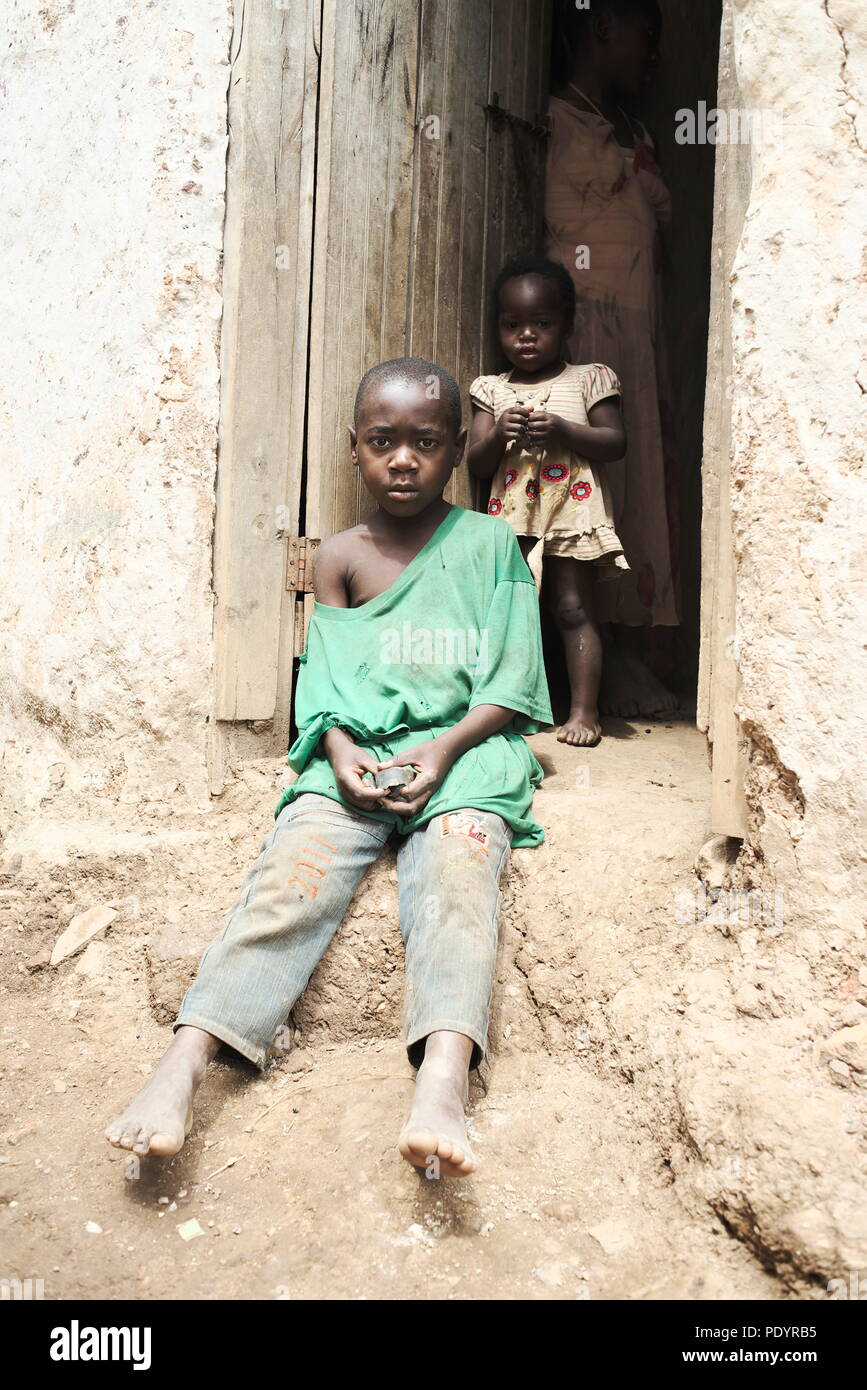 a poor under dressed Young Ugandan child sits in a doorway of a temporary mountain home in Southwest Uganda Stock Photo