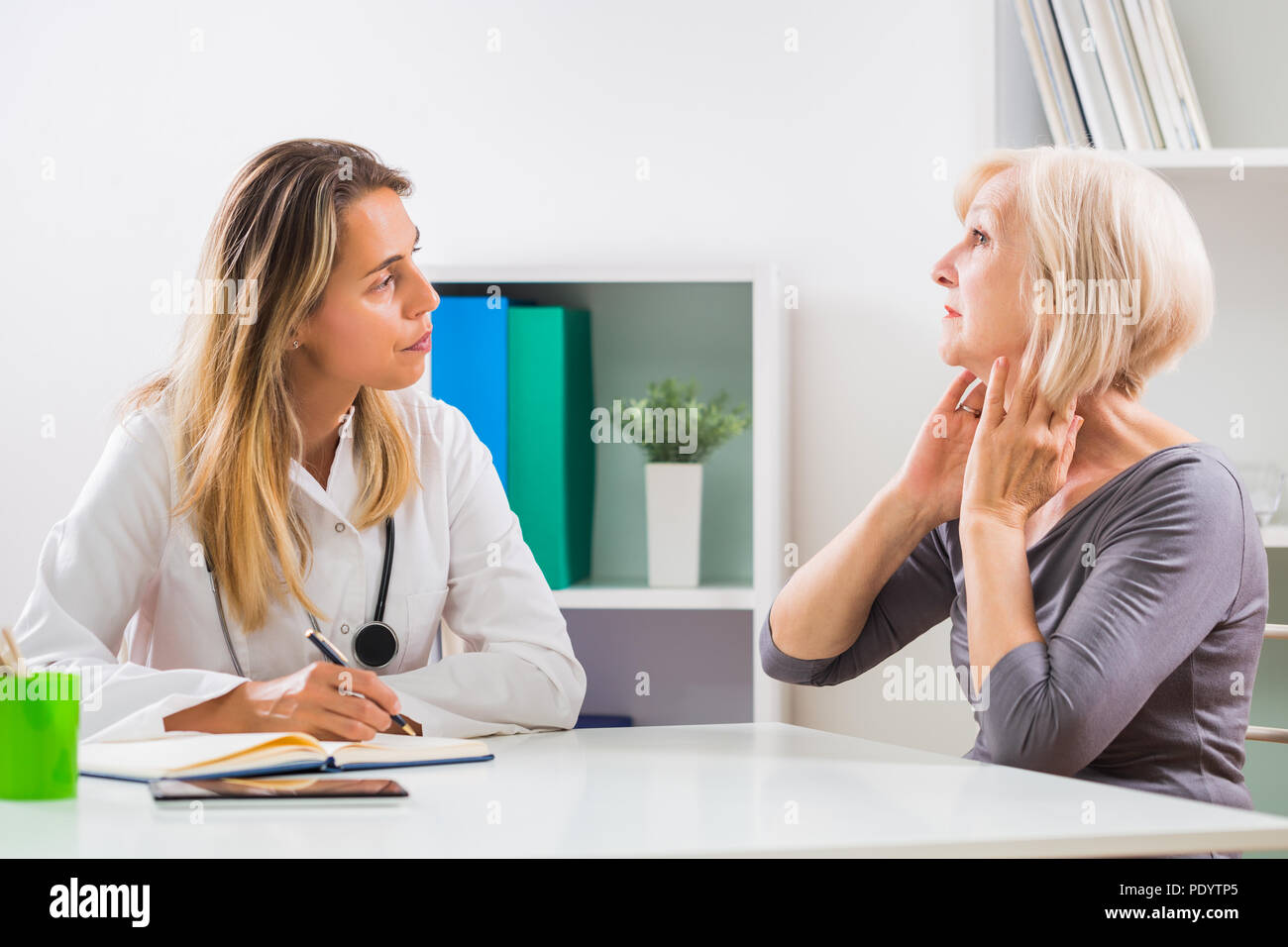 Senior patient telling female doctor how she is having problems with her throat. Stock Photo