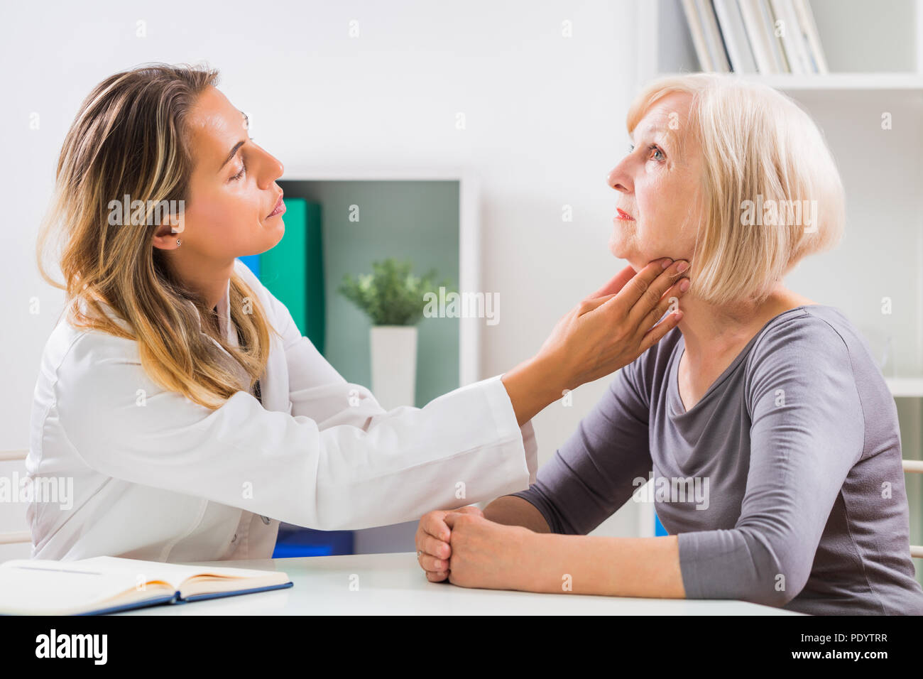 Female doctor examines her senior patient's throat in office. Stock Photo