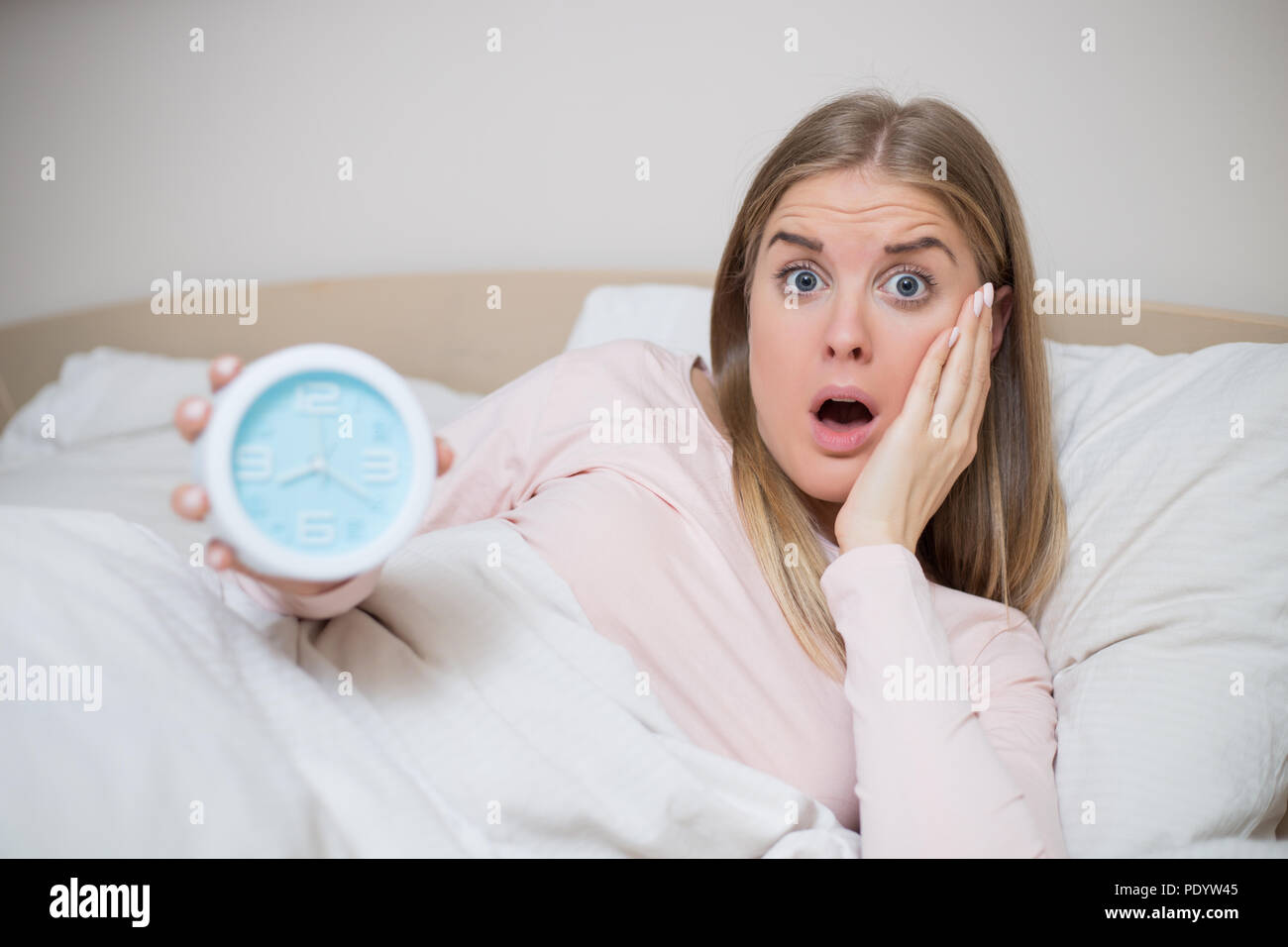 Terrified woman holding alarm clock. Stock Photo