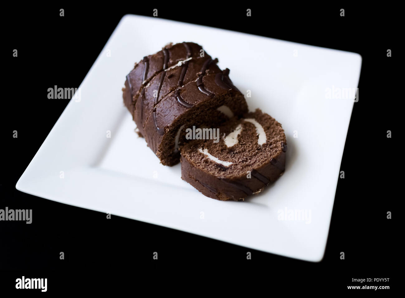 chocolate roll in icing on a white plate wooden table Stock Photo