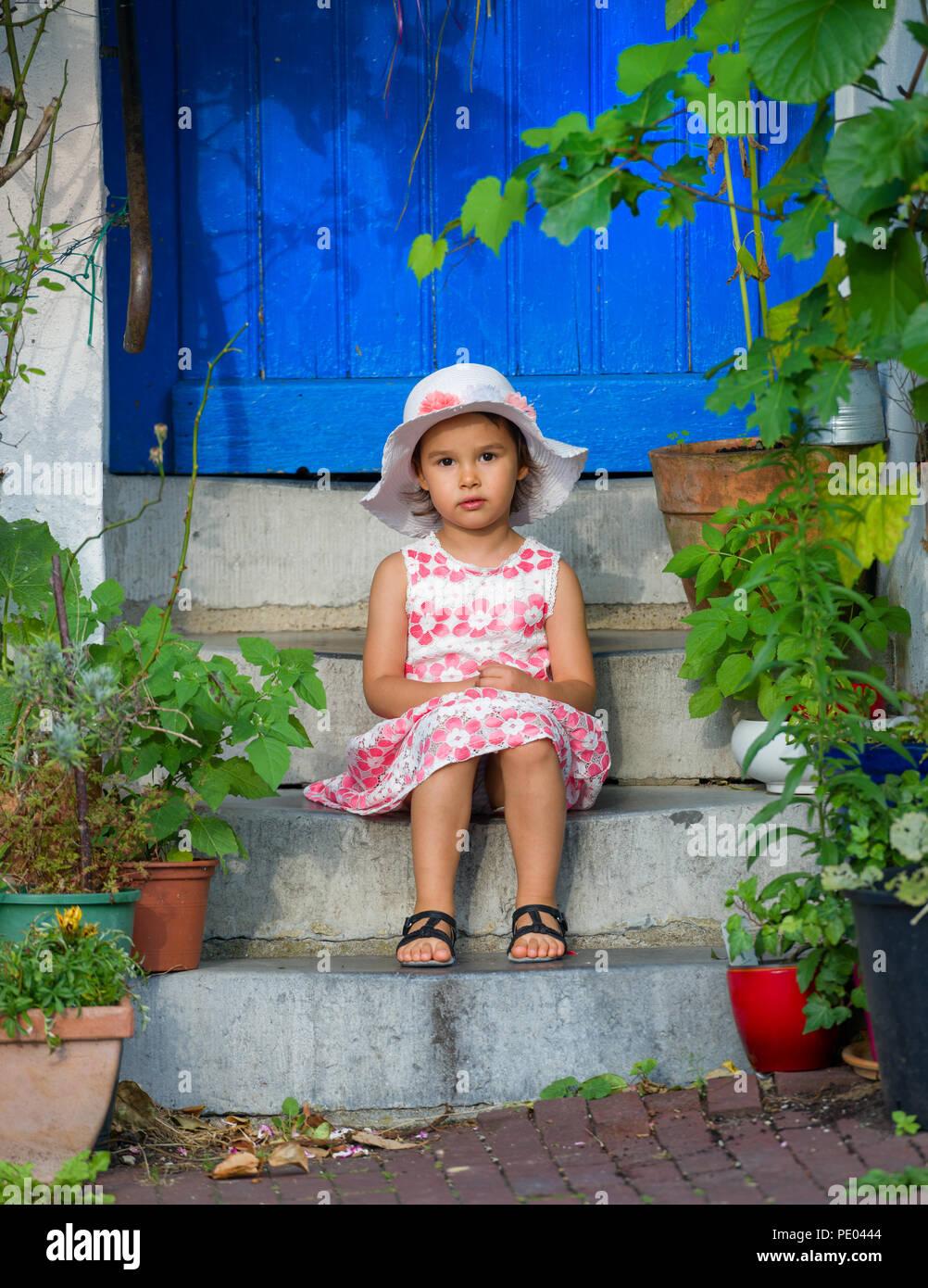 Adorable little girl wearing white hat  sitting on stairs on warm and sunny summer day Stock Photo