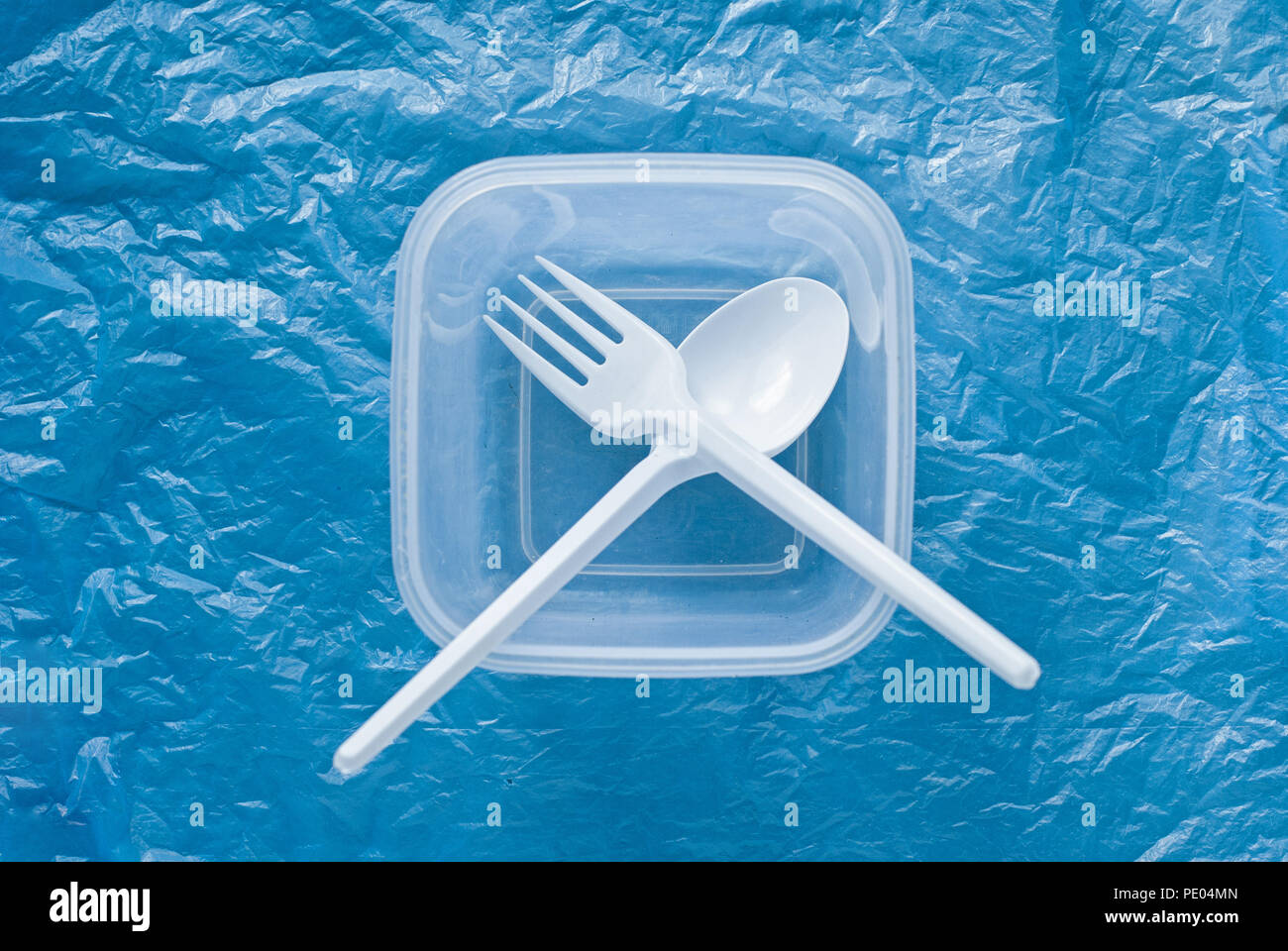 white plastic spoon and fork in a plastic container on a blue plastic bag Stock Photo