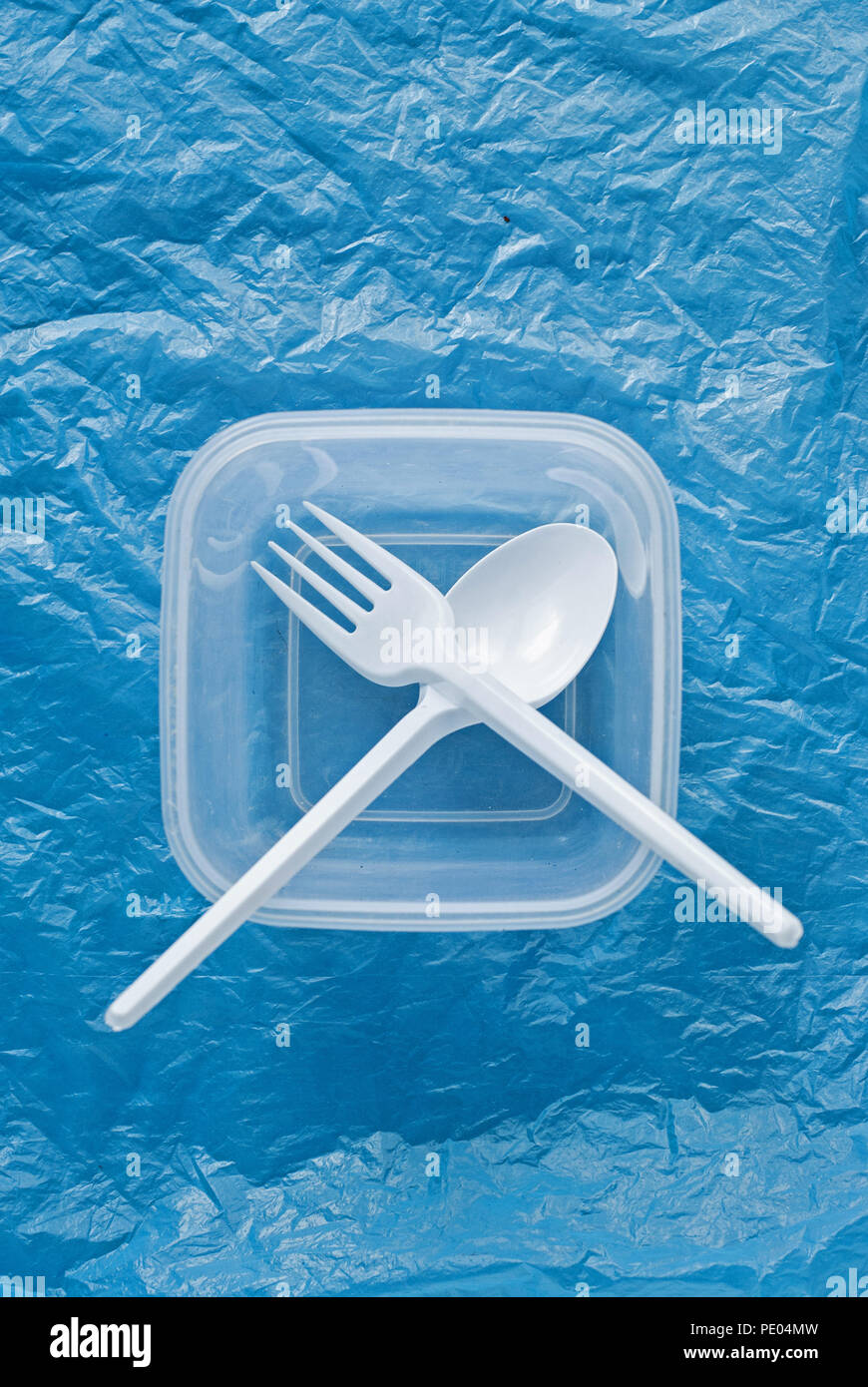 white plastic spoon and fork in a plastic container on a blue plastic bag Stock Photo
