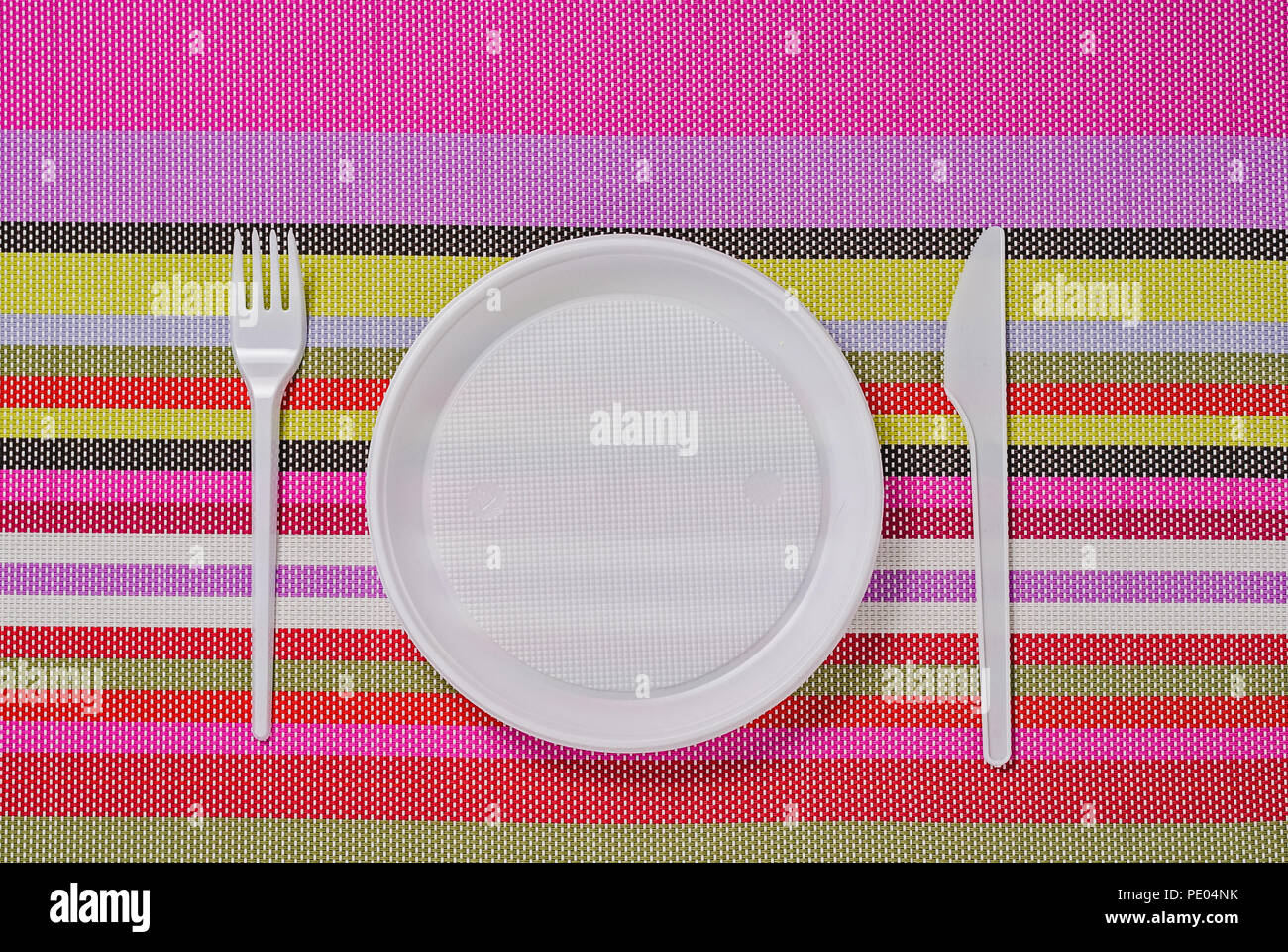 white plastic utensils, fork, plate and knife on a colored striped napkin Stock Photo