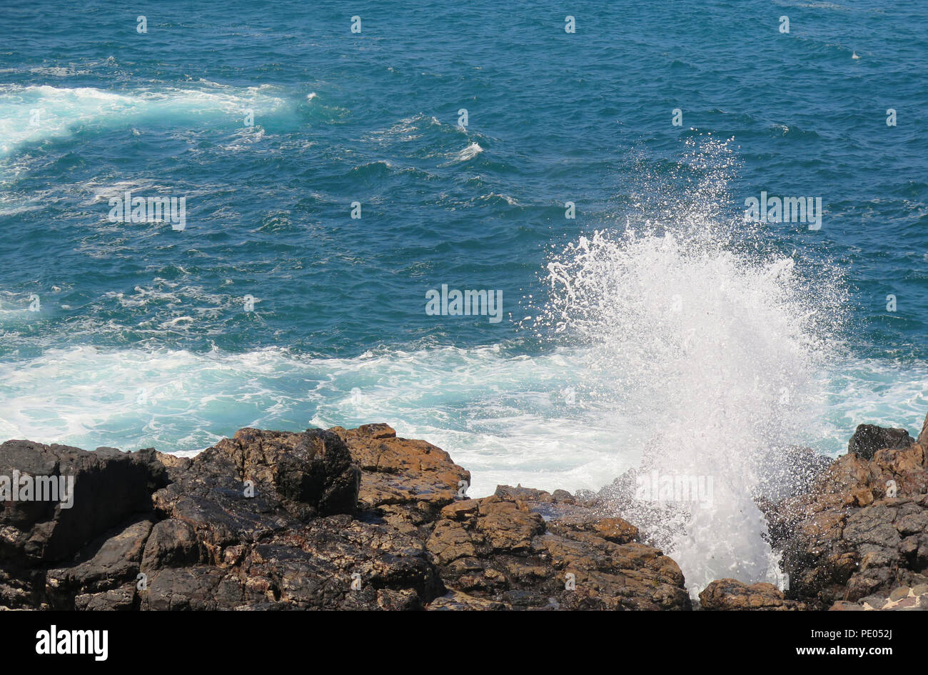 Waves crashing on rocks in bright sunshine Stock Photo