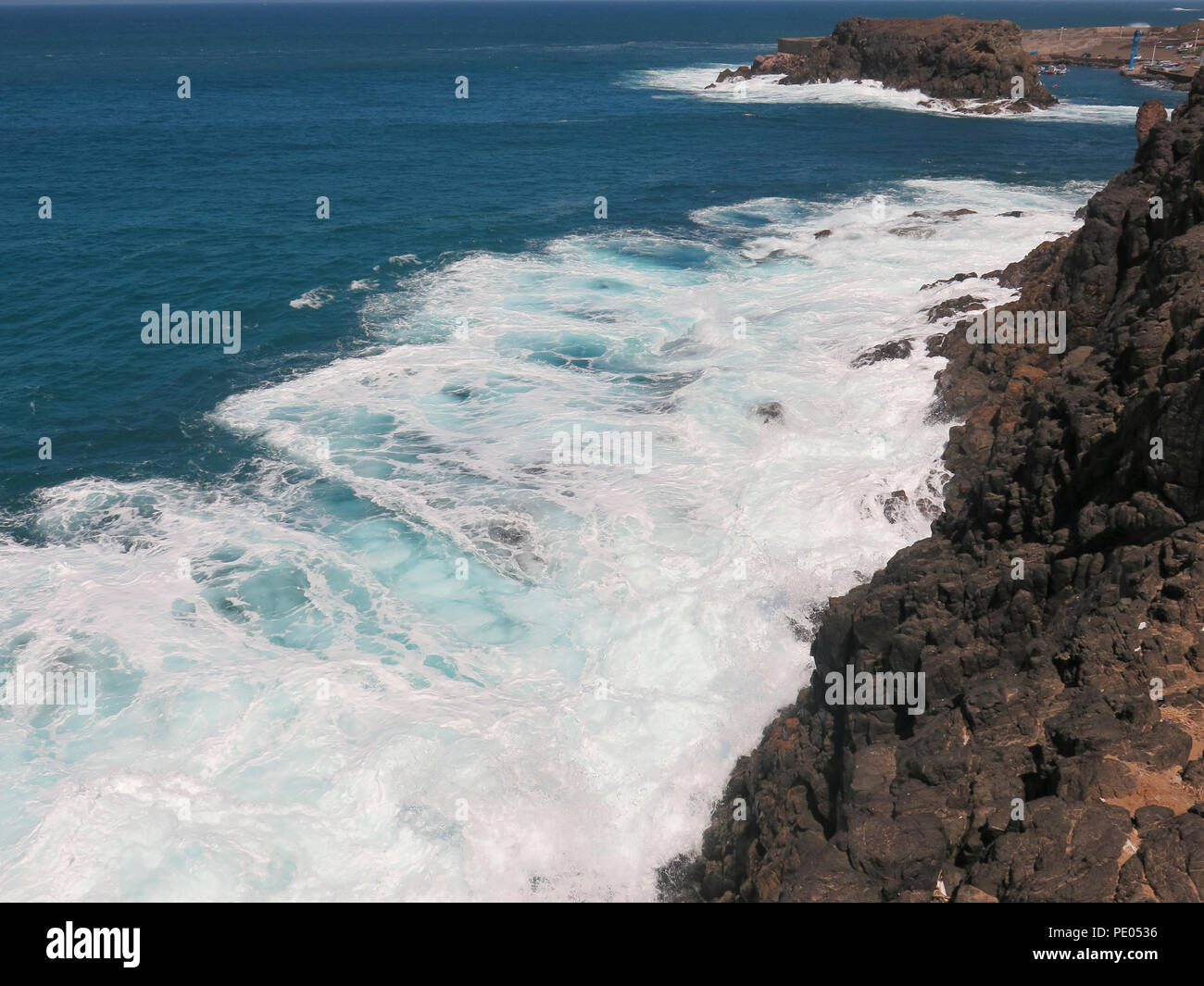 Waves crashing on rocks in bright sunshine Stock Photo