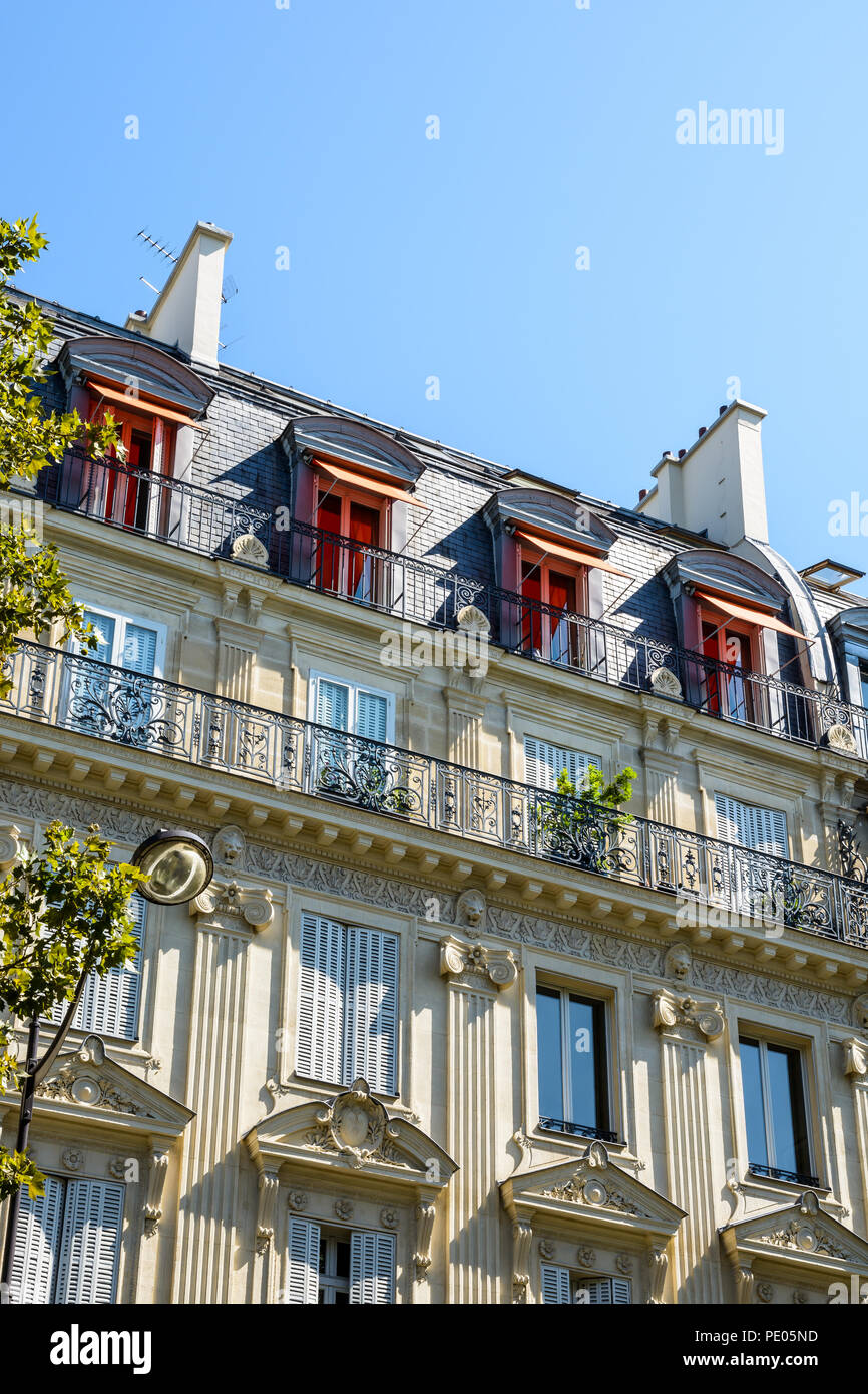View from down the street of a typical parisian, opulent-looking building of haussmannian style with cut stone facade, carved ornaments and balcony. Stock Photo