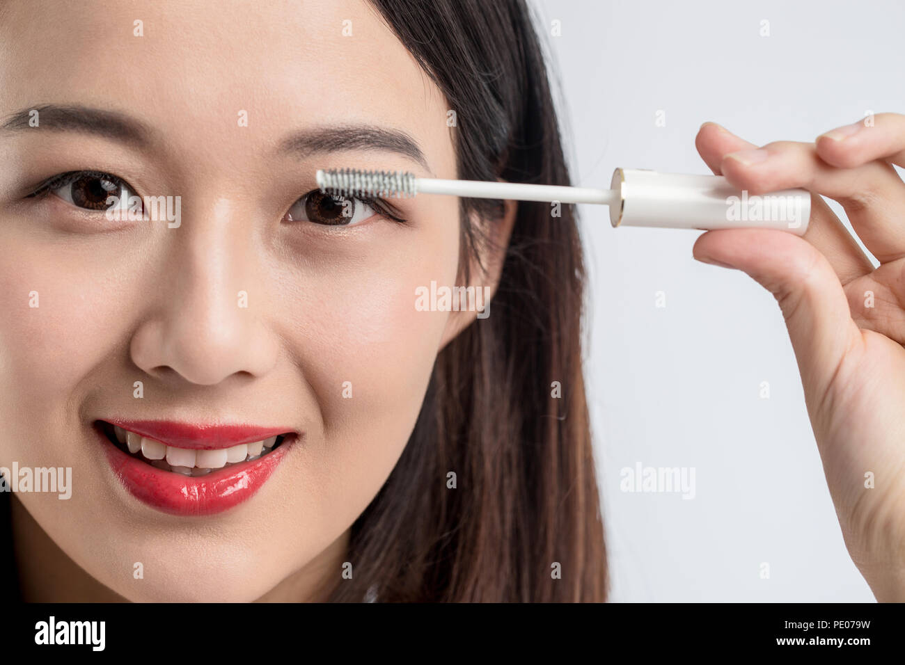 Chinese woman putting mascara on eyelashes on gray background Stock Photo -  Alamy