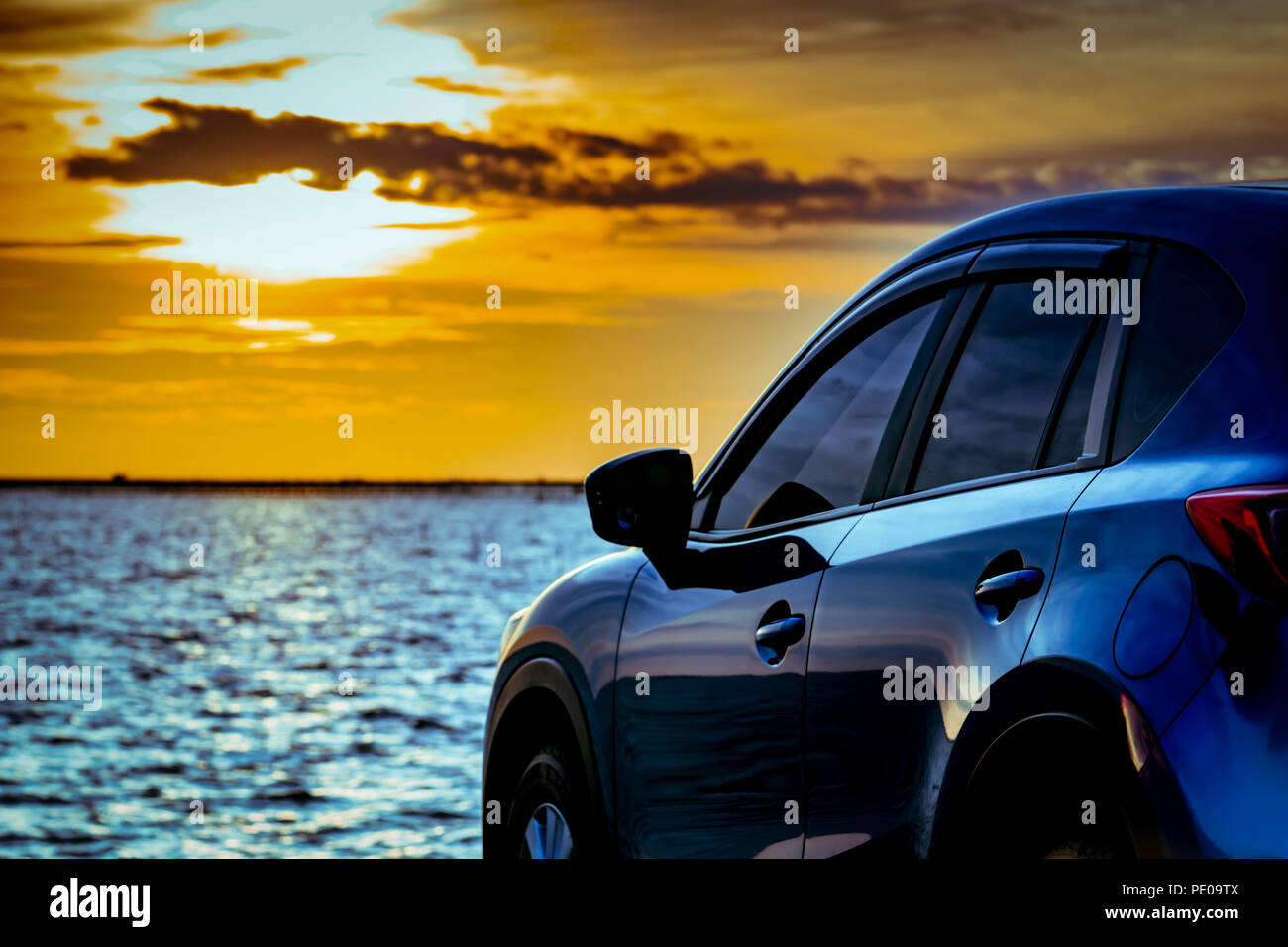 Blue compact SUV car with sport and modern design parked on concrete road by the sea at sunset. Environmentally friendly technology. Electric car tech Stock Photo