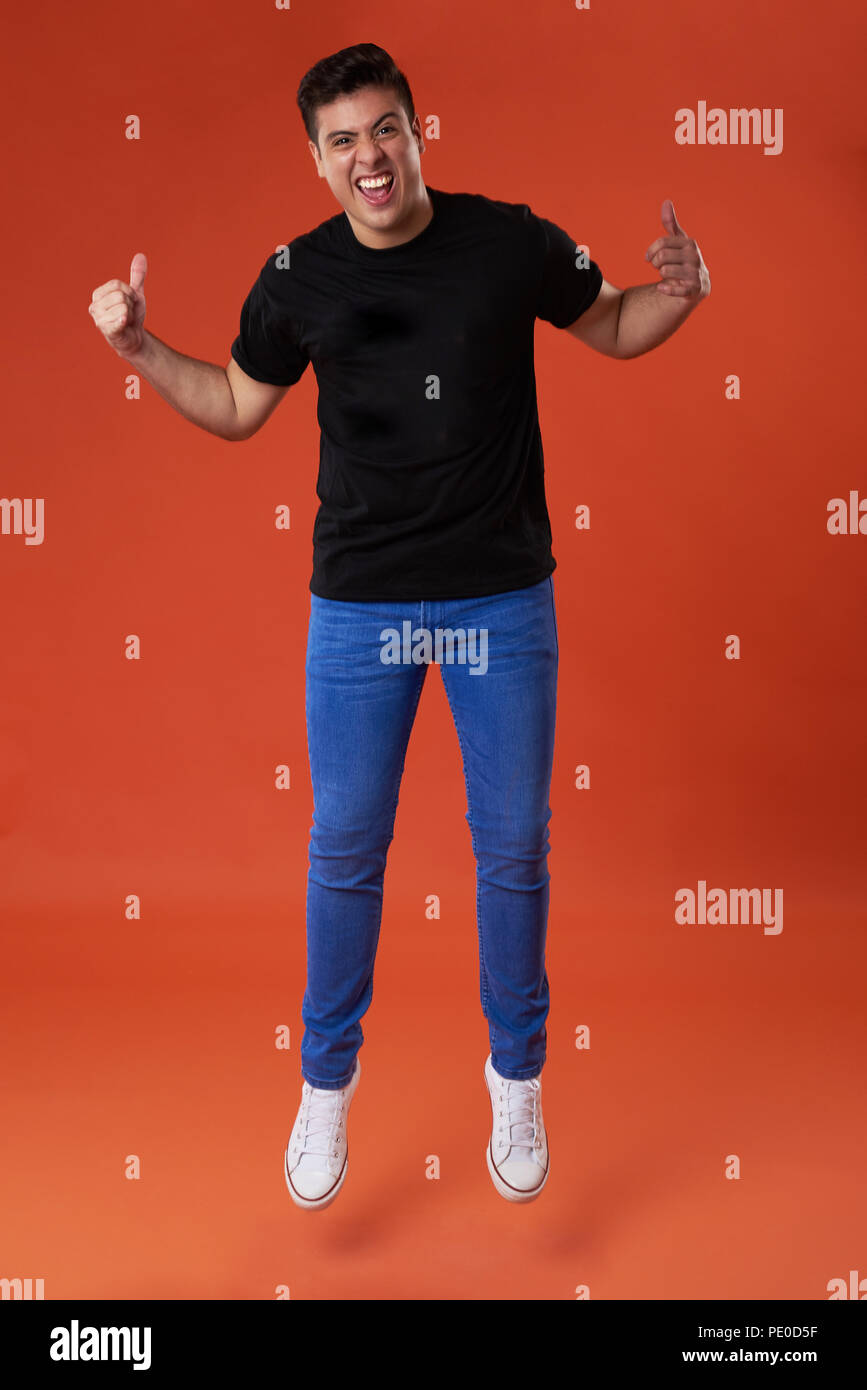 Jumping man with thumb up in orange studio background Stock Photo