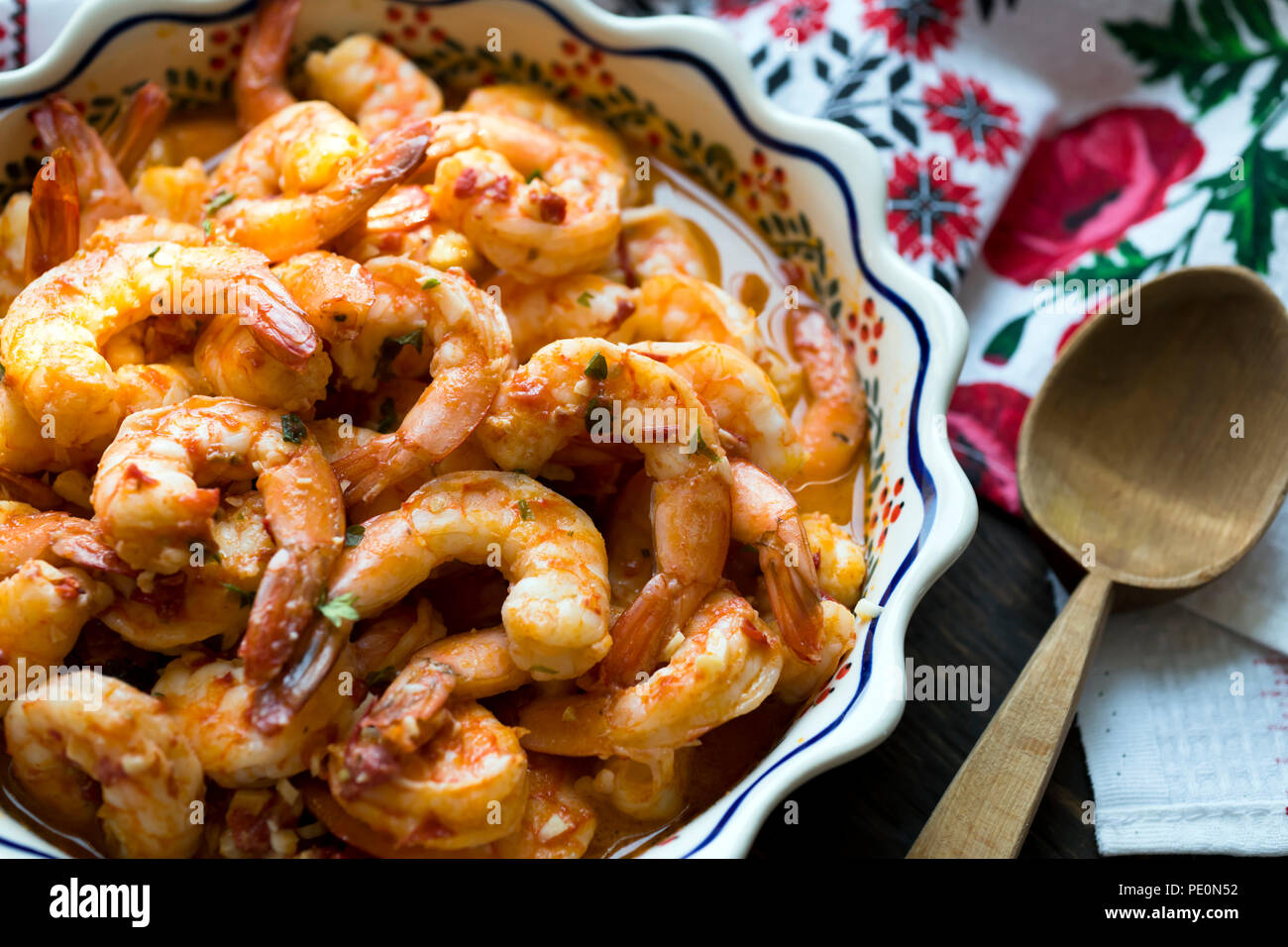 Spicy appetizing seafood Shrimps cooked and baked in sauce are displayed on a wooden table in a dish with ornament located next to a towel with colorf Stock Photo