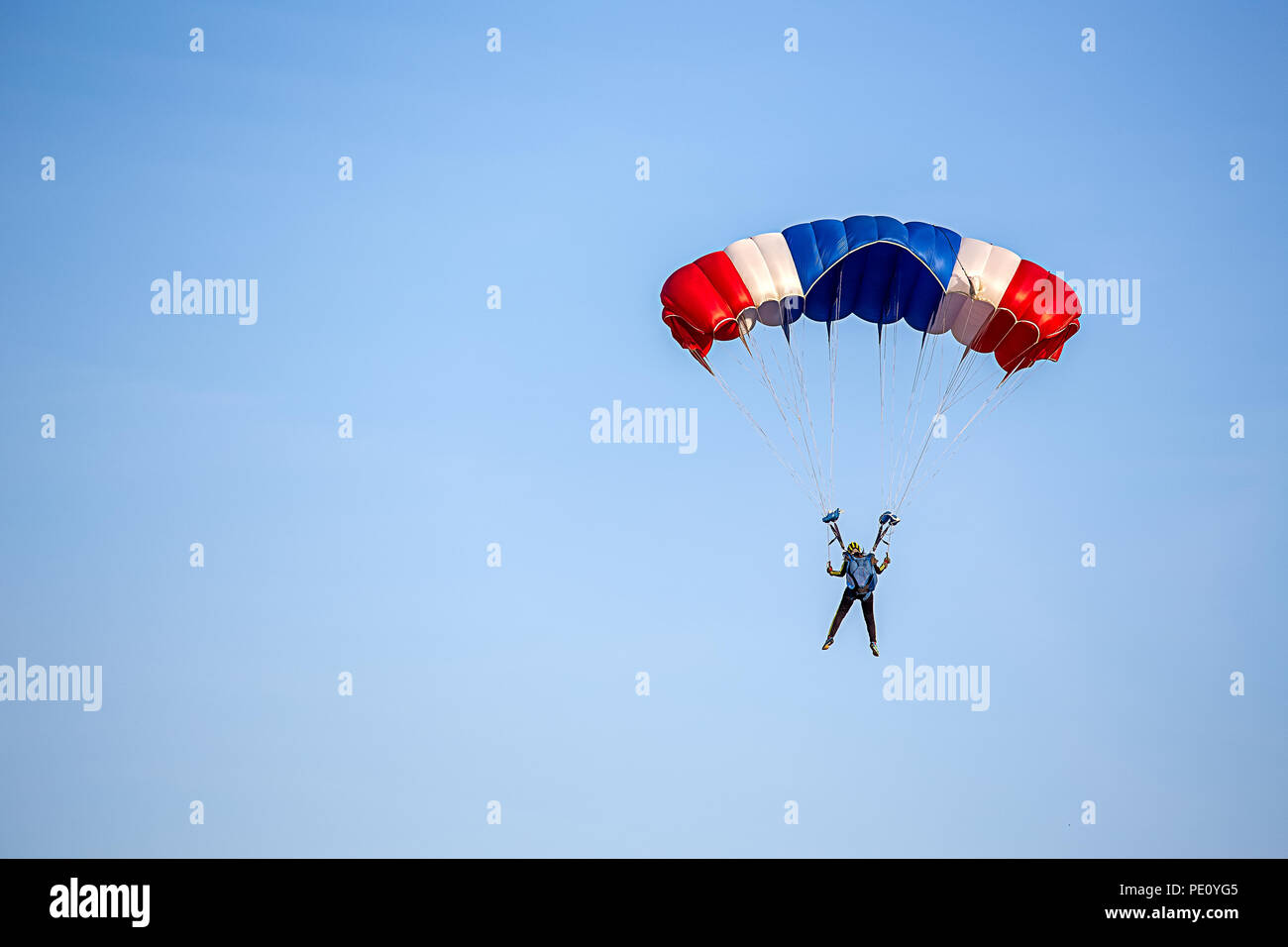 isolated skydiver in colorful parachute gliding after free fall jump with blue sky background