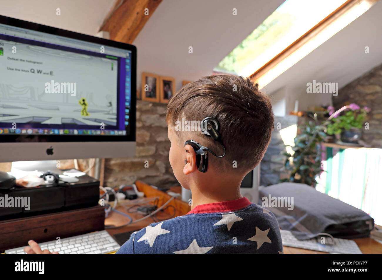 Rear back view of boy child with digital technology cochlear implants looking at screen playing a computer game at home in the UK    KATHY DEWITT Stock Photo