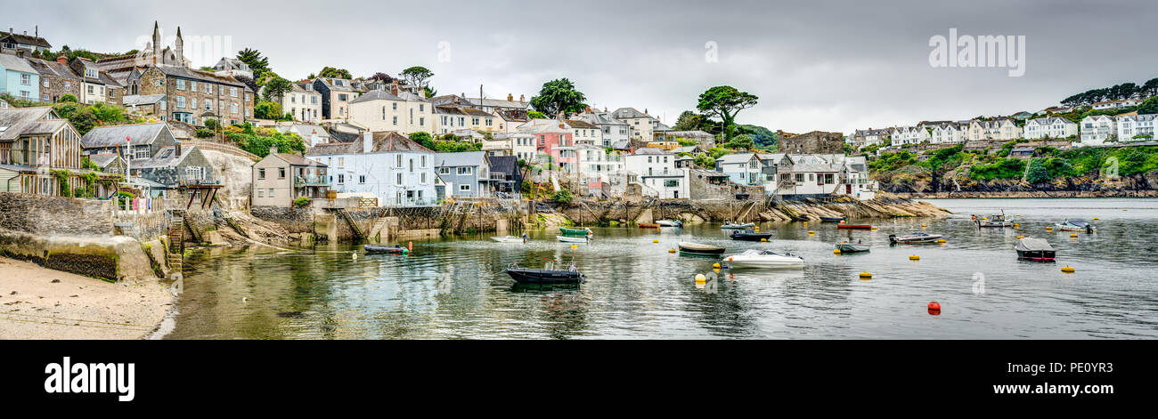 A wide colourful panoramic of a beautiful Cornish seaside harbour village Polruan on the Fowey Estuary. Calm waters and small boats in safe mooring. Stock Photo