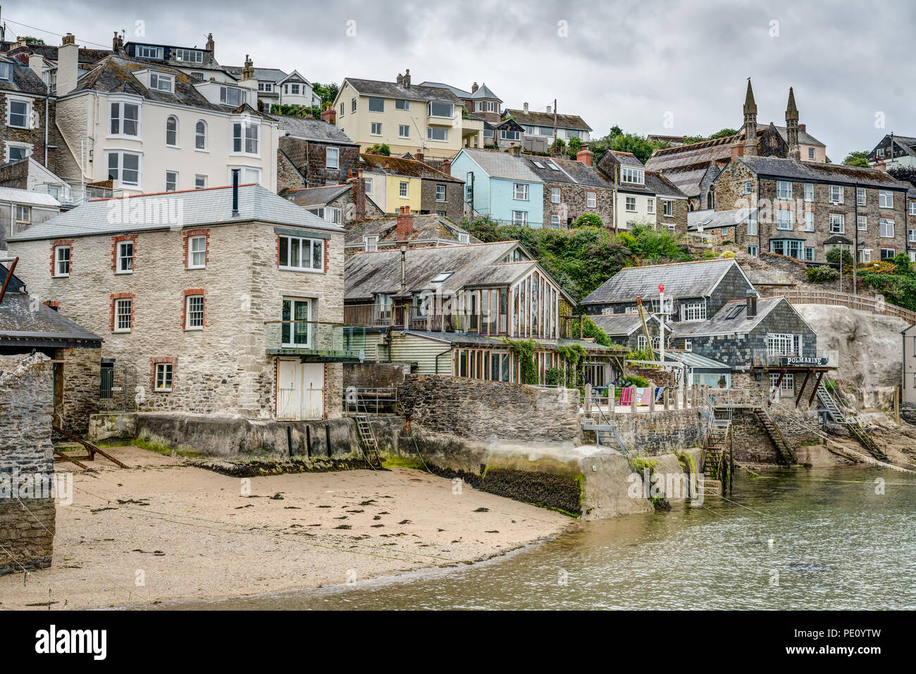 A typical Cornish landscape picture of the small beach at Polruan quayside on the Fowey Estuary surrounded by old marine buildings and village homes. Stock Photo