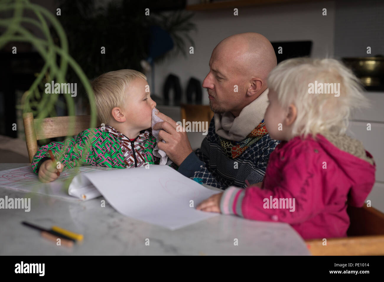Father cleaning boys mouth in living room Stock Photo