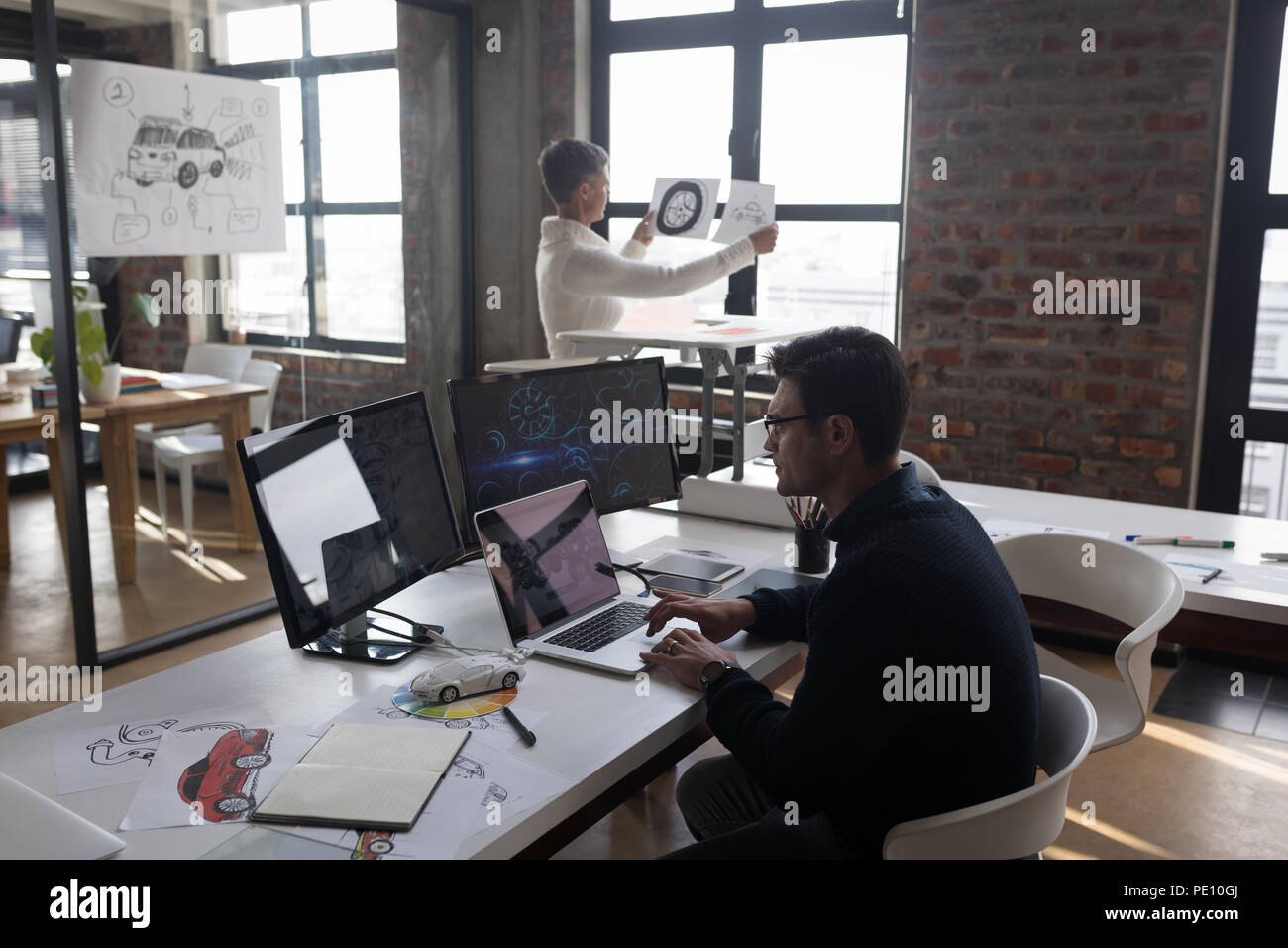 Businessman using laptop while his colleagues looking at sketch Stock Photo