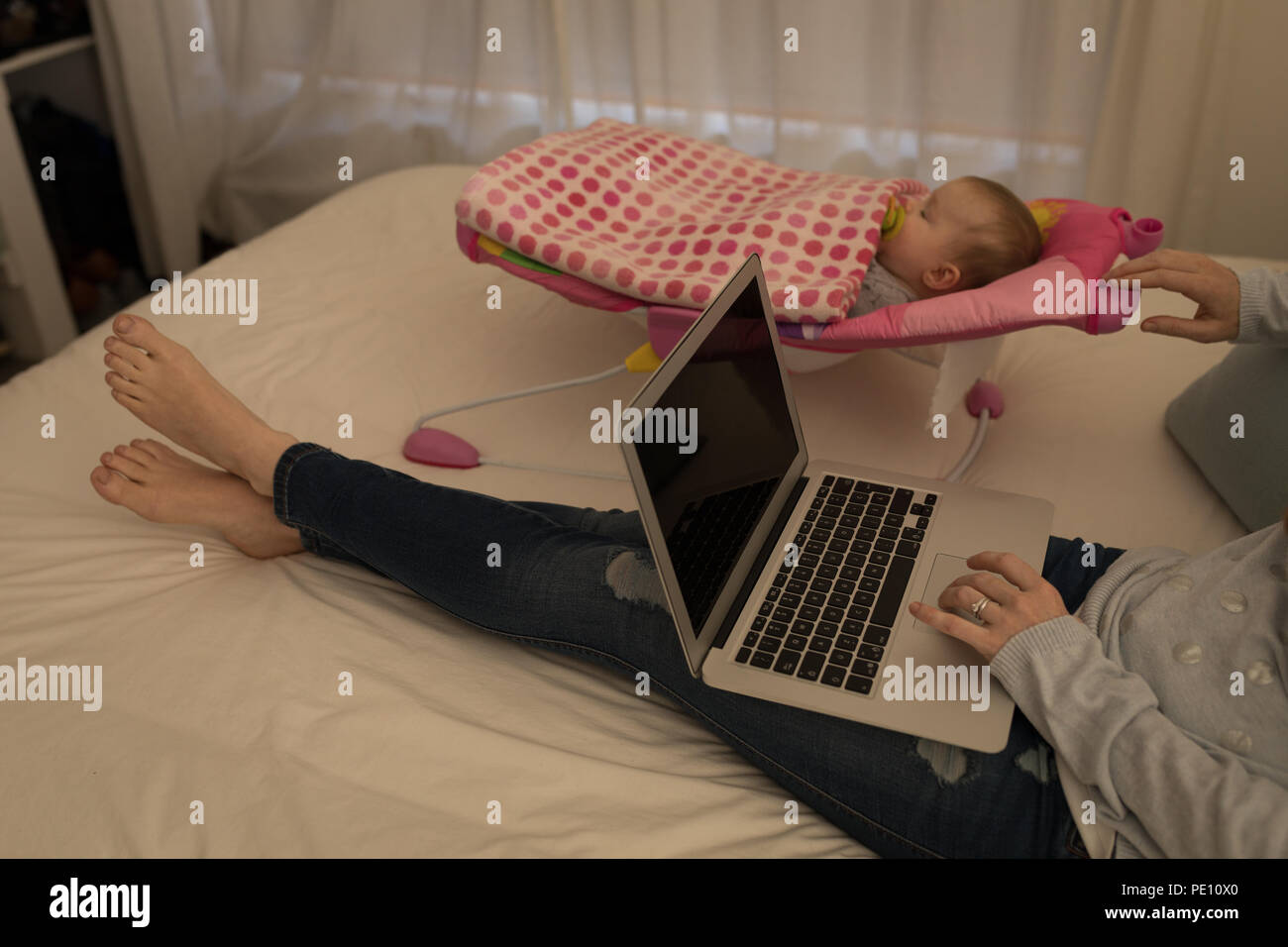 Mother using laptop while her baby boy sleeping Stock Photo