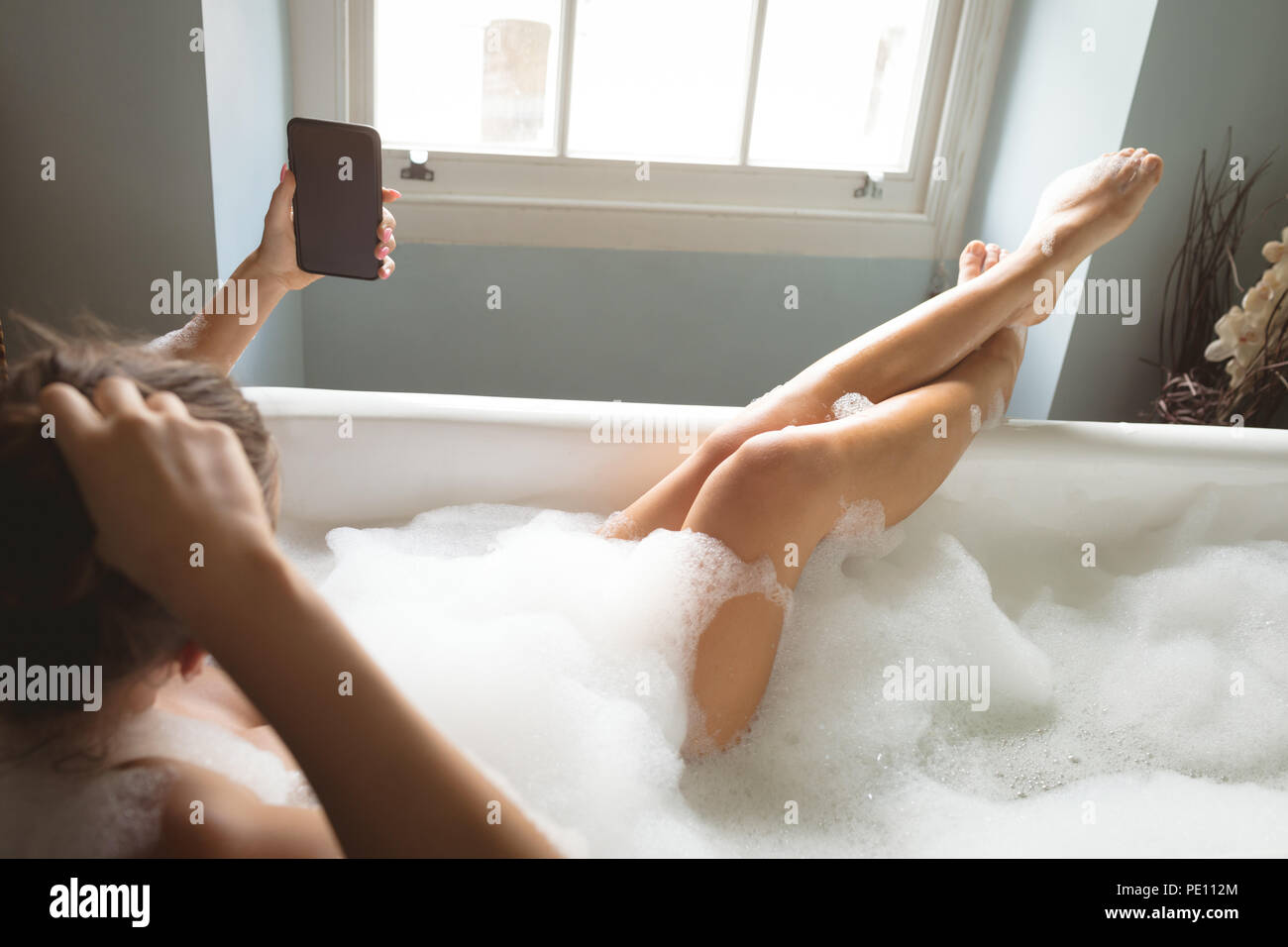 Woman using mobile phone while taking a bath in bath tub Stock Photo