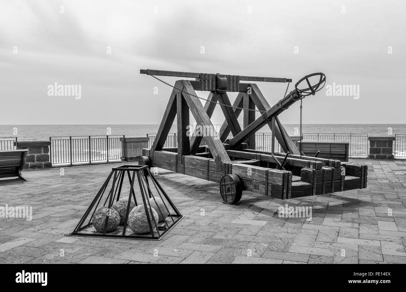 ancient catapult on the ramparts of Alghero ,Sardinia Island, Italy , Defensive wall. Catapult in the downtown of the citywith the sea as background and the big stone bullets in front Stock Photo