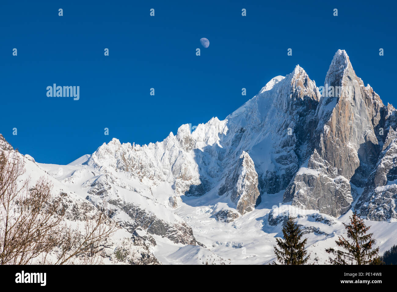 The moon against a deep blue sky above the mountains near Chamonix.  Chardonnay and and Les Drus are covered in snow.  Taken from Montroc Stock Photo