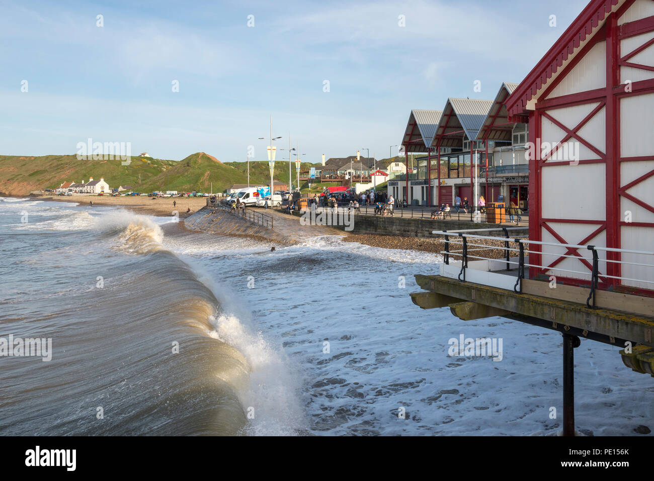 Waves breaking against the promenade at Saltburn-by-the-sea, North Yorkshire, England. A sunny spring afternoon with lots of people enjoying the view. Stock Photo