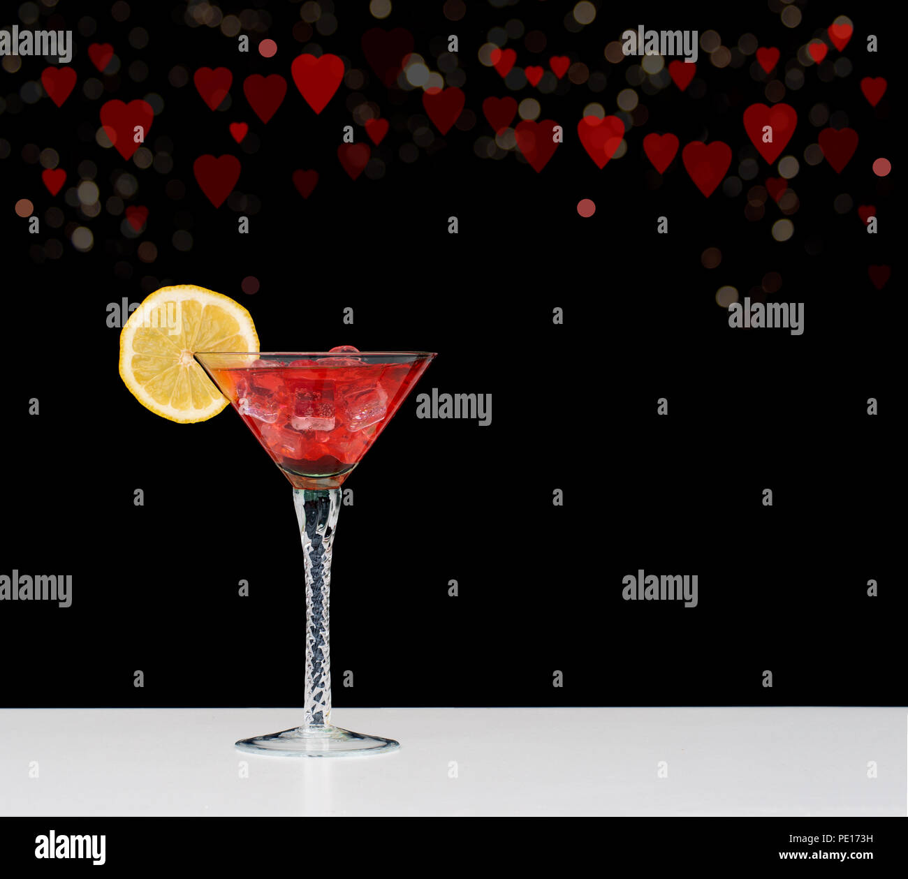 Romantic pink cocktail with ice, lemon and fresh raspberries. Triangular glass on white with black background behind with bokeh of hearts and circles. Stock Photo
