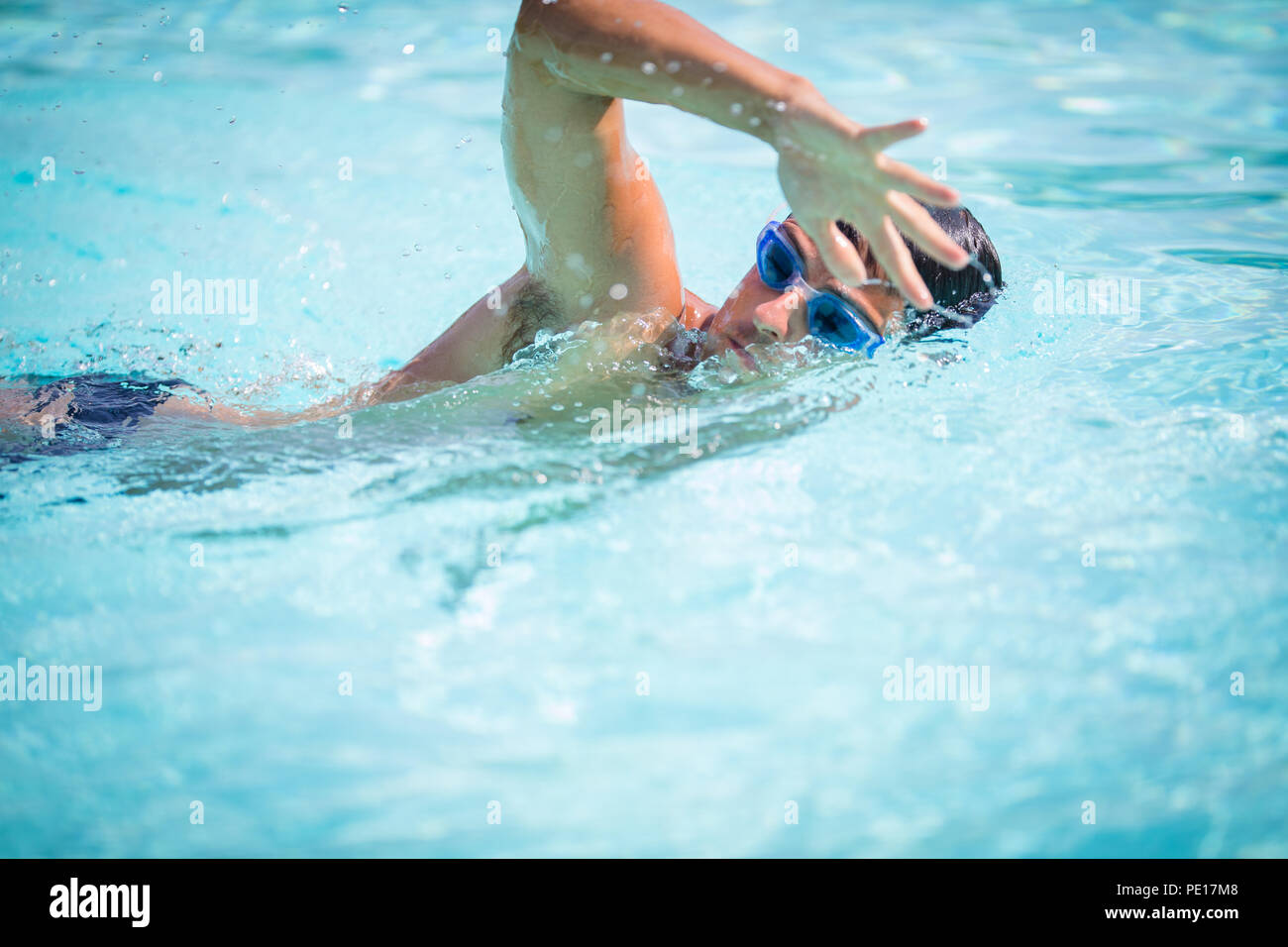 Man swimmer swimming crawl in a blue water  pool. Portrait of an athletic young male triathlete swimming crawl wearing swimming goggles. Triathlete tr Stock Photo