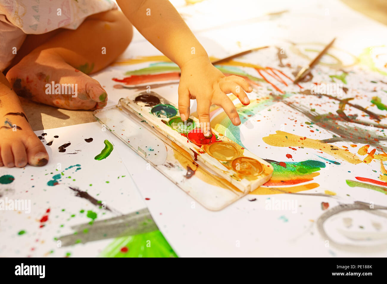 A Little Girl With Curly Hair Sits On The Floor And Paints