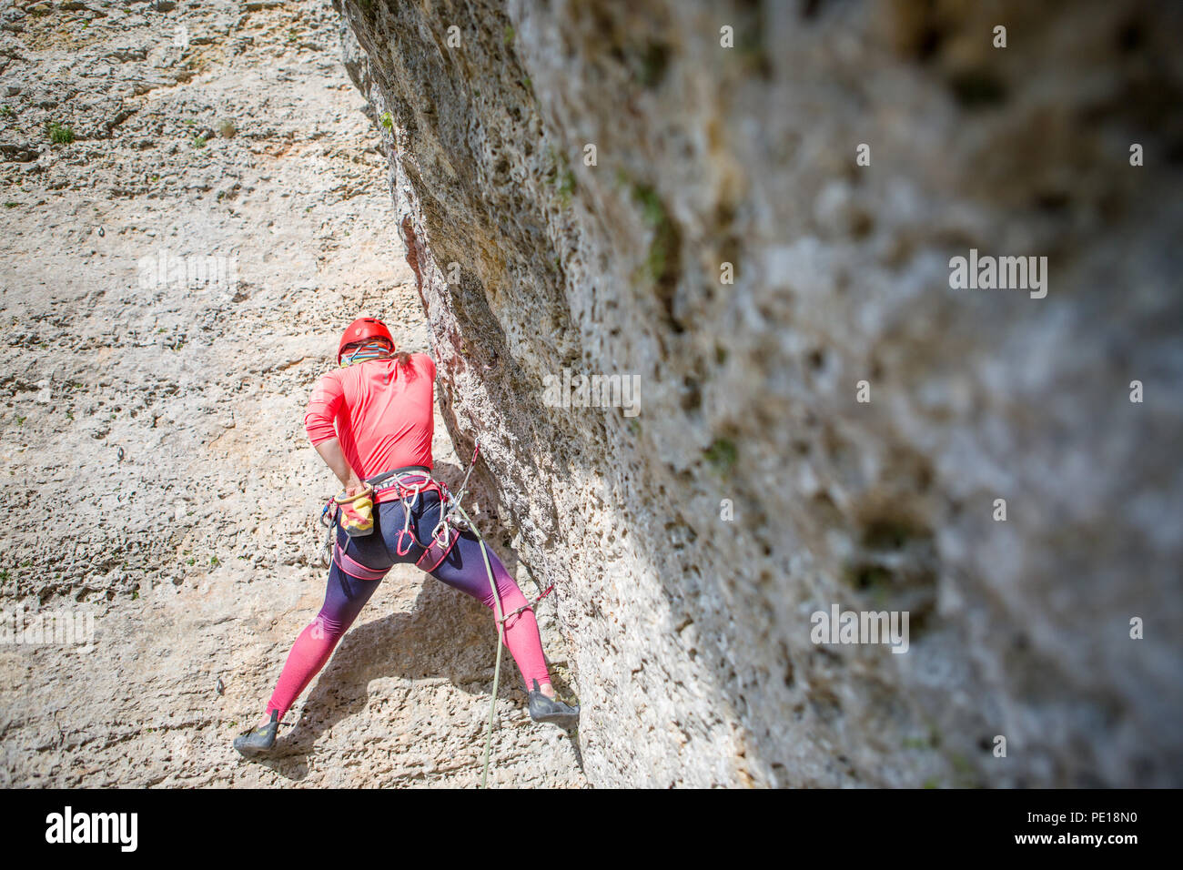 Photo of sports woman in red hard hat with carbine in hand climbing