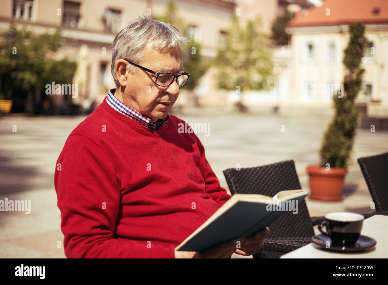 Senior man enjoys reading book and drinking coffee at the bar. Stock Photo