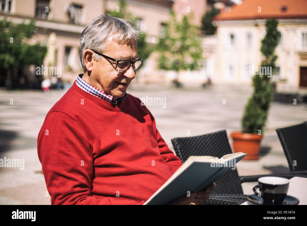 Senior man enjoys reading book and drinking coffee at the bar. Stock Photo