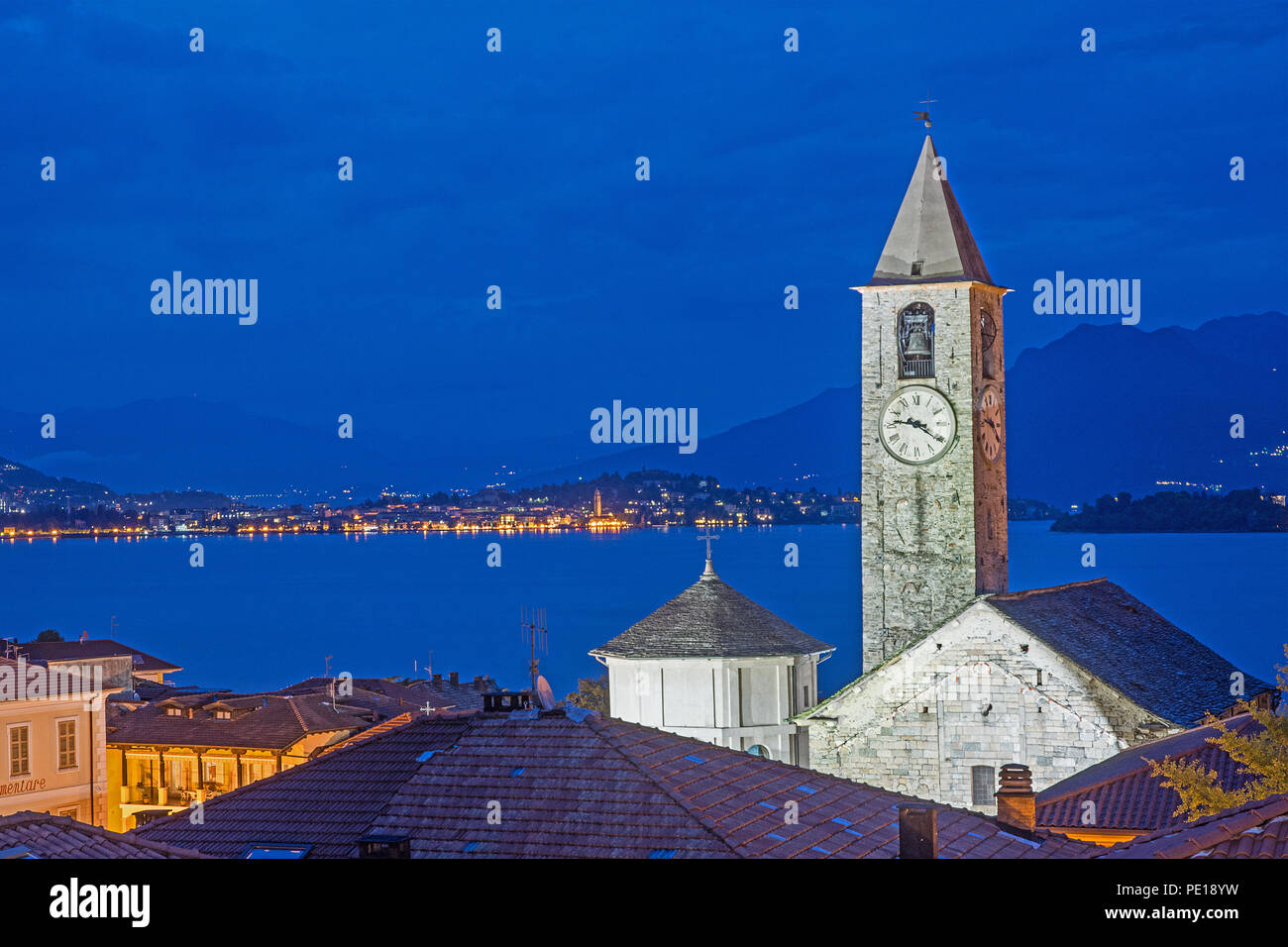 Blue hour view from roof top terrace of Hotel Rosa Baveno Italy with view of church clock tower and Lago Maggiore showing floodlit church and sparklin Stock Photo