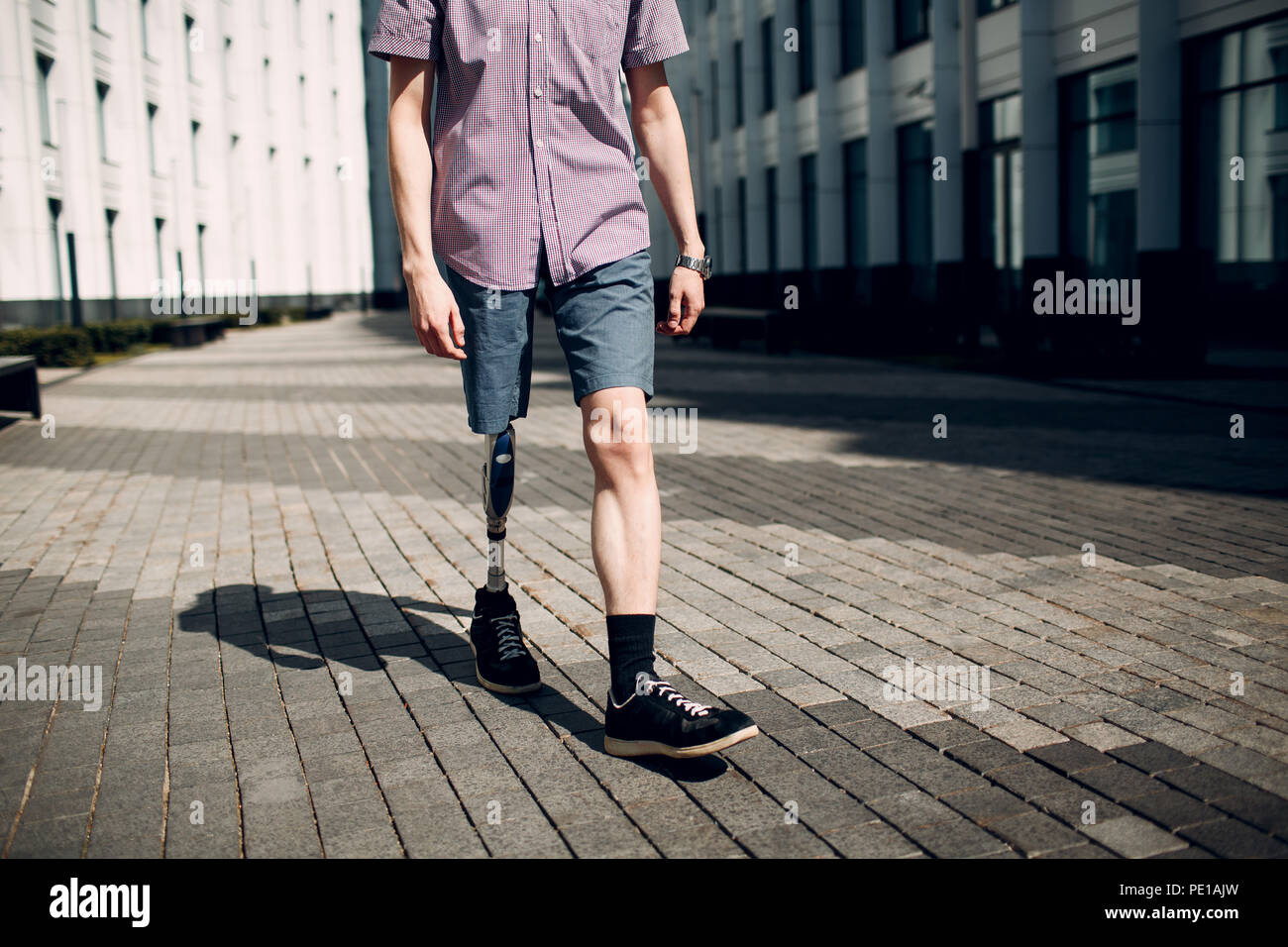 Disabled young man with foot prosthesis walks along the street. Stock Photo