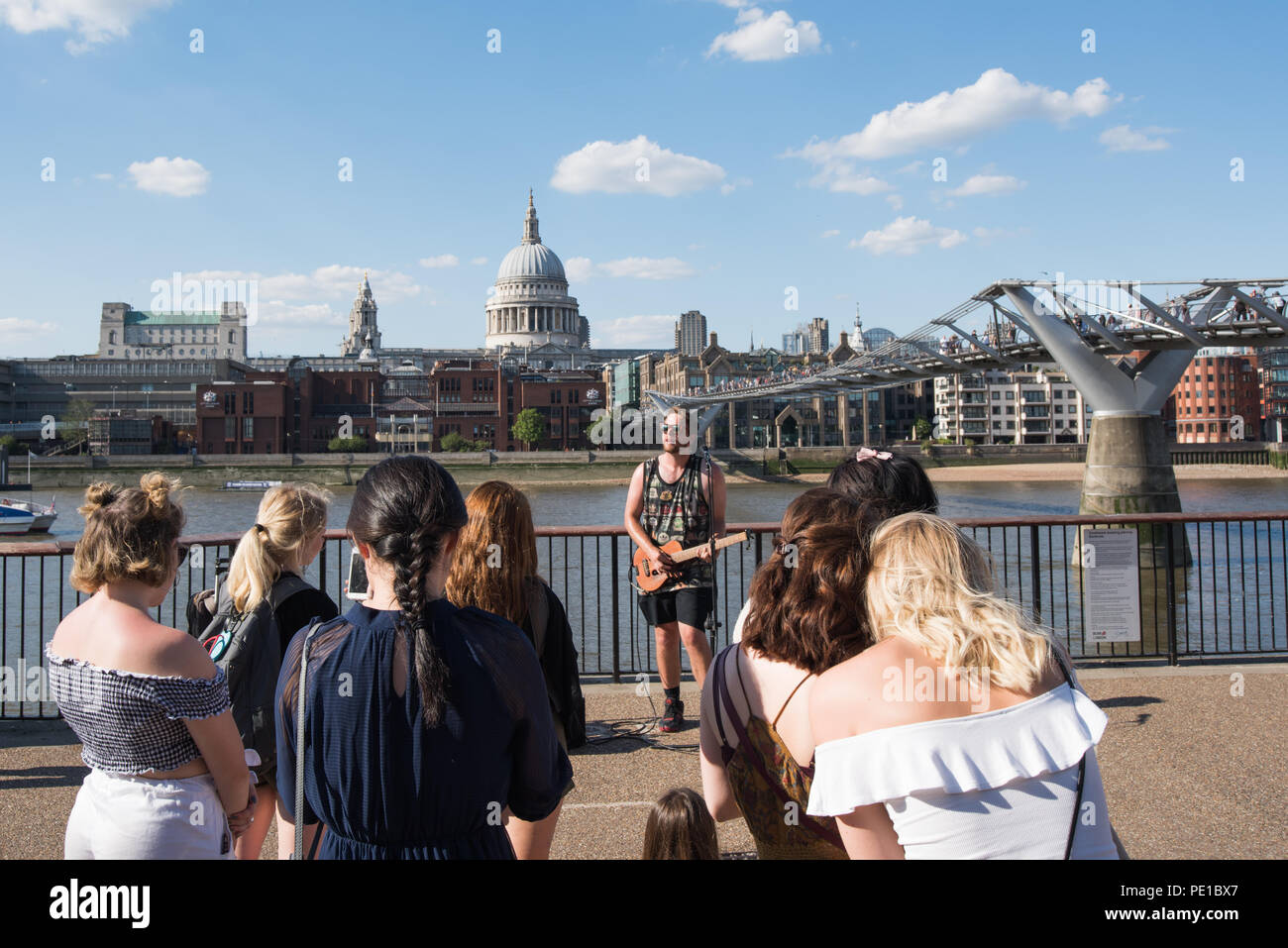 Street performance / Busker playing guitar with young girls audience on the London south bank with St.Pauls cathedral and Millennium bridge Stock Photo