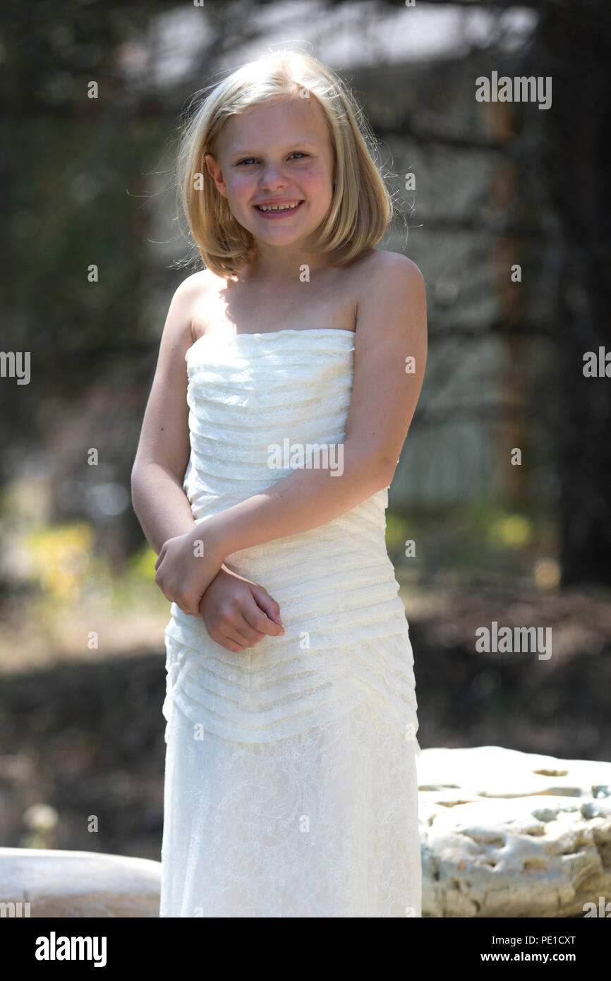 Fantasy, 8-9 year attractie blonde, wearing aunt's wedding dress. Standing outdoors smilimg at camera. Stock Photo