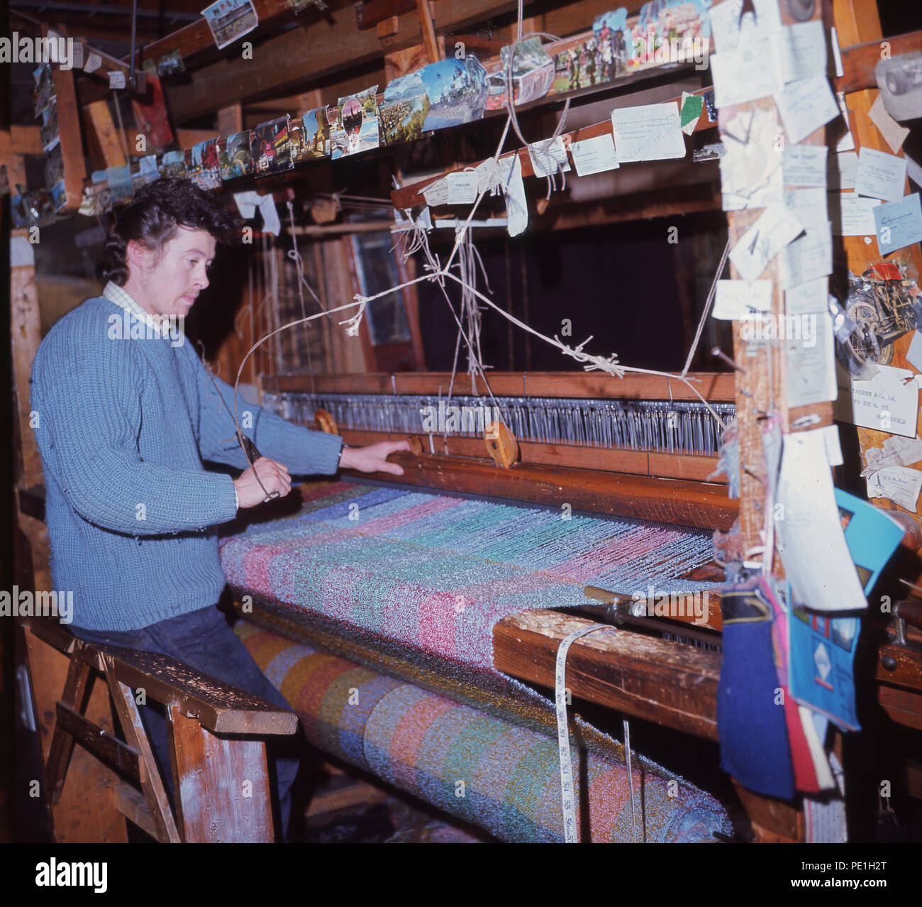 1960s, man weaving mohair cloth by hand on a wooden loom, Grasmere, Cumbria. A silk-life fabric or yarn, mohair is made from the hair of the Angora goat and as can be seen takes dyes well, to produce vibrant colourful garments. Stock Photo