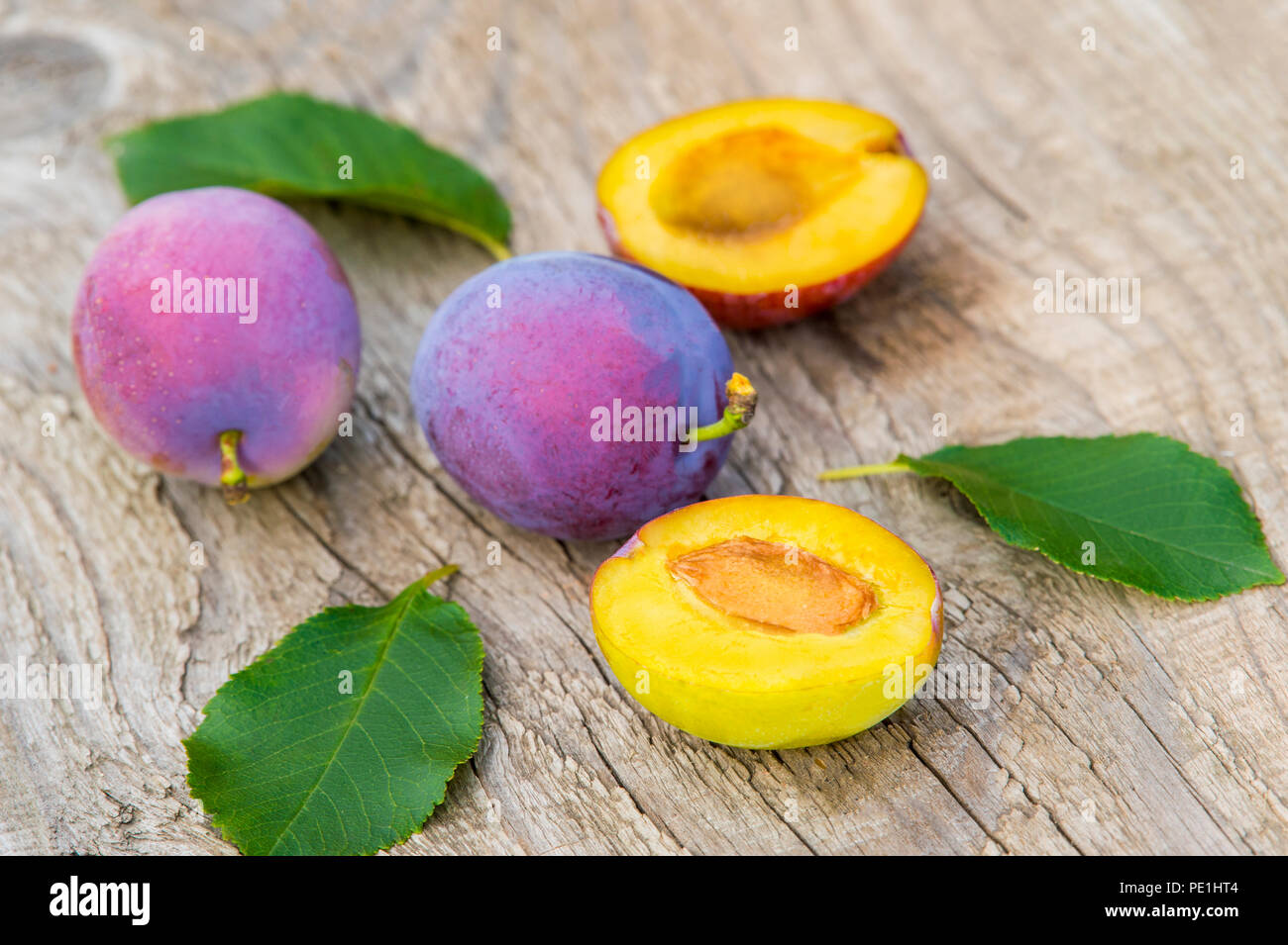 ripe plums with leaves on old wooden background Stock Photo