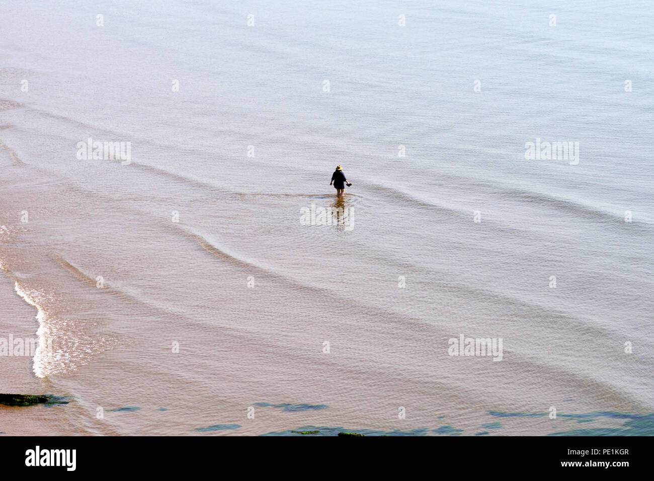 A lone holiday maker paddling in the sea at low tide. Stock Photo