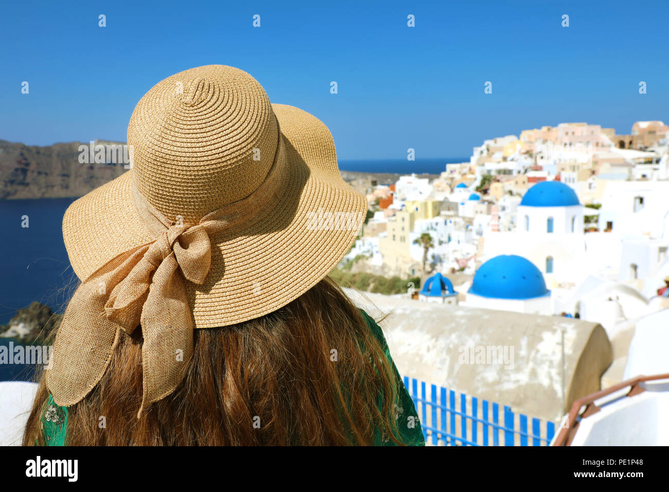 Back view of woman with hat in Santorini looking at white village houses with blue domes, Cyclades, Greece, Europe Stock Photo