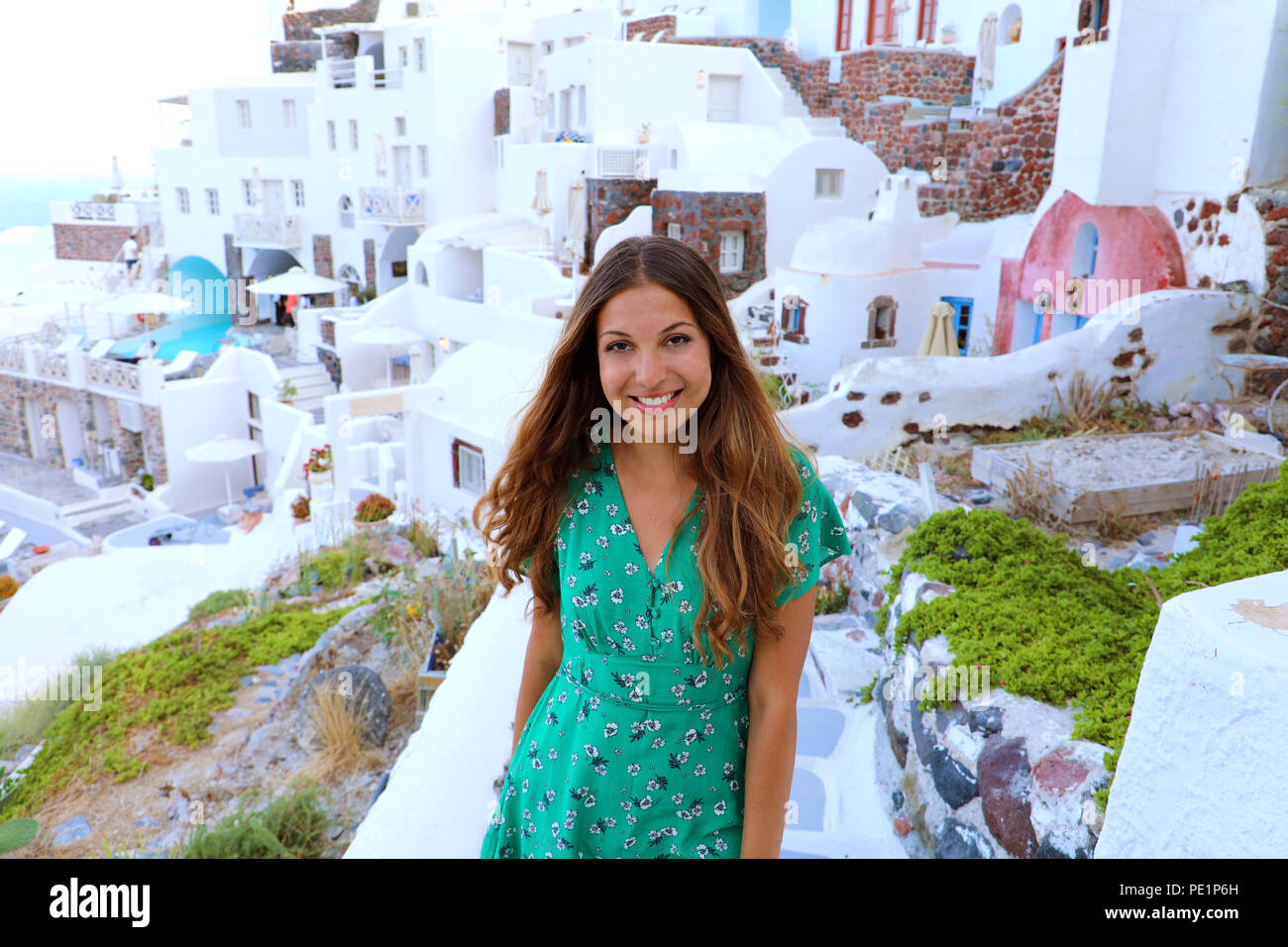 Santorini travel tourist woman visiting famous white village of Oia. Smiling tanned girl in green dress climbs the stairs in Santorini, Cyclades, Gree Stock Photo