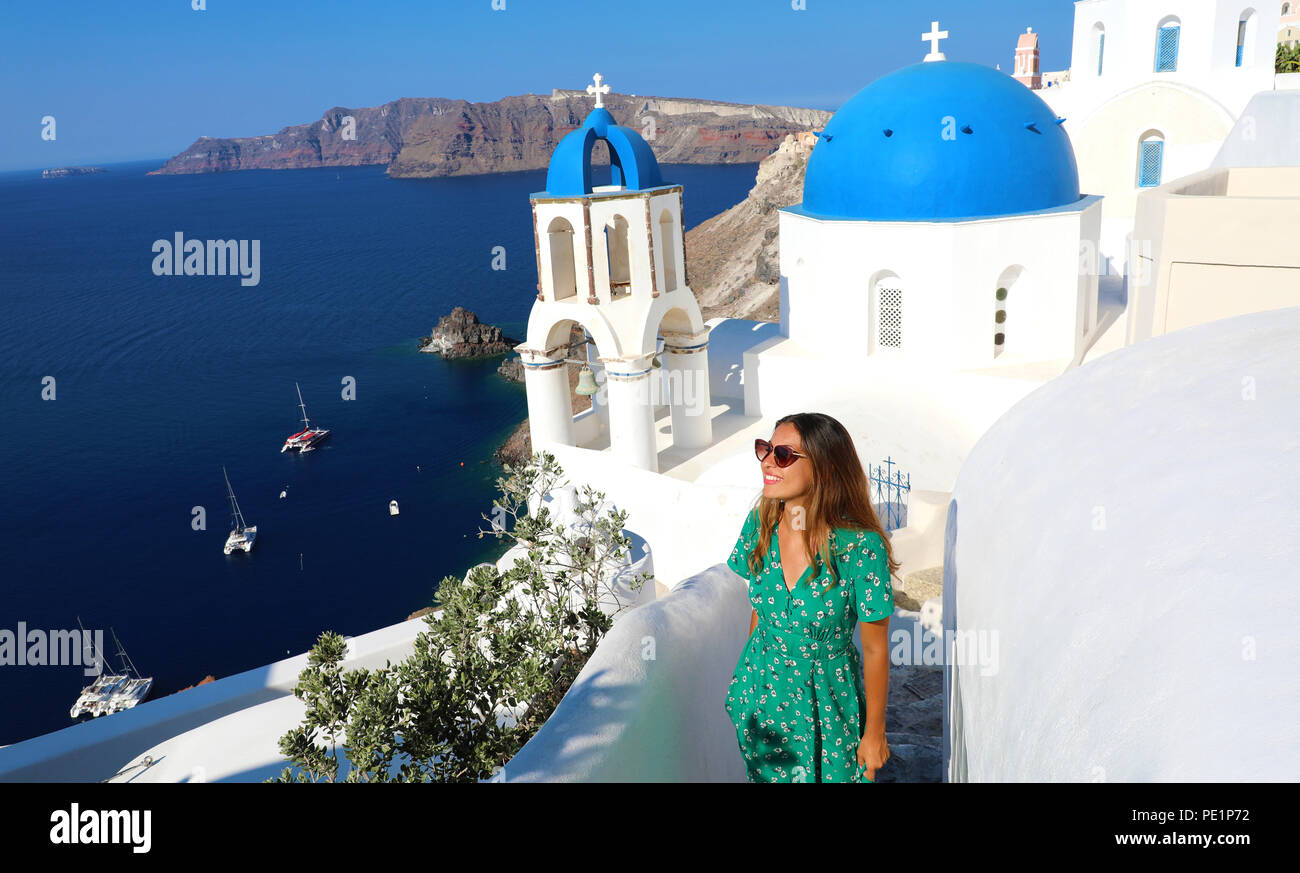 Santorini fashion woman visiting Oia, famous white village with blue domes in Greece. Girl in green dress and sunglasses looking to the side faboulos Stock Photo