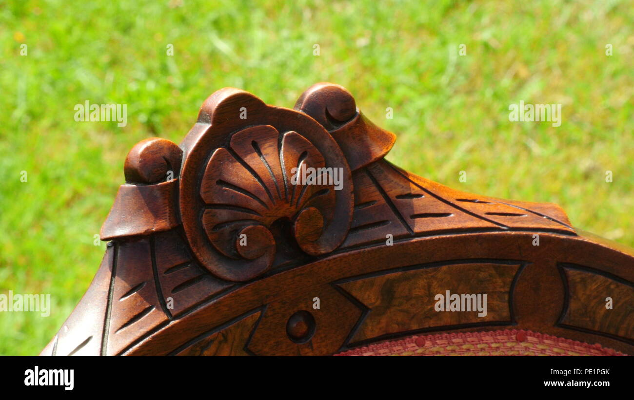 A unique top of a mahogany antique wooden chair with vintage flower motifs carved into it, close-up on green background Stock Photo