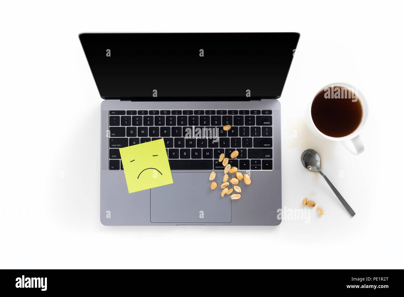 Top view of tabletop with messy dirty laptop, post it notes with sad face, nuts, spoon and coffee cup isolated on white background Stock Photo